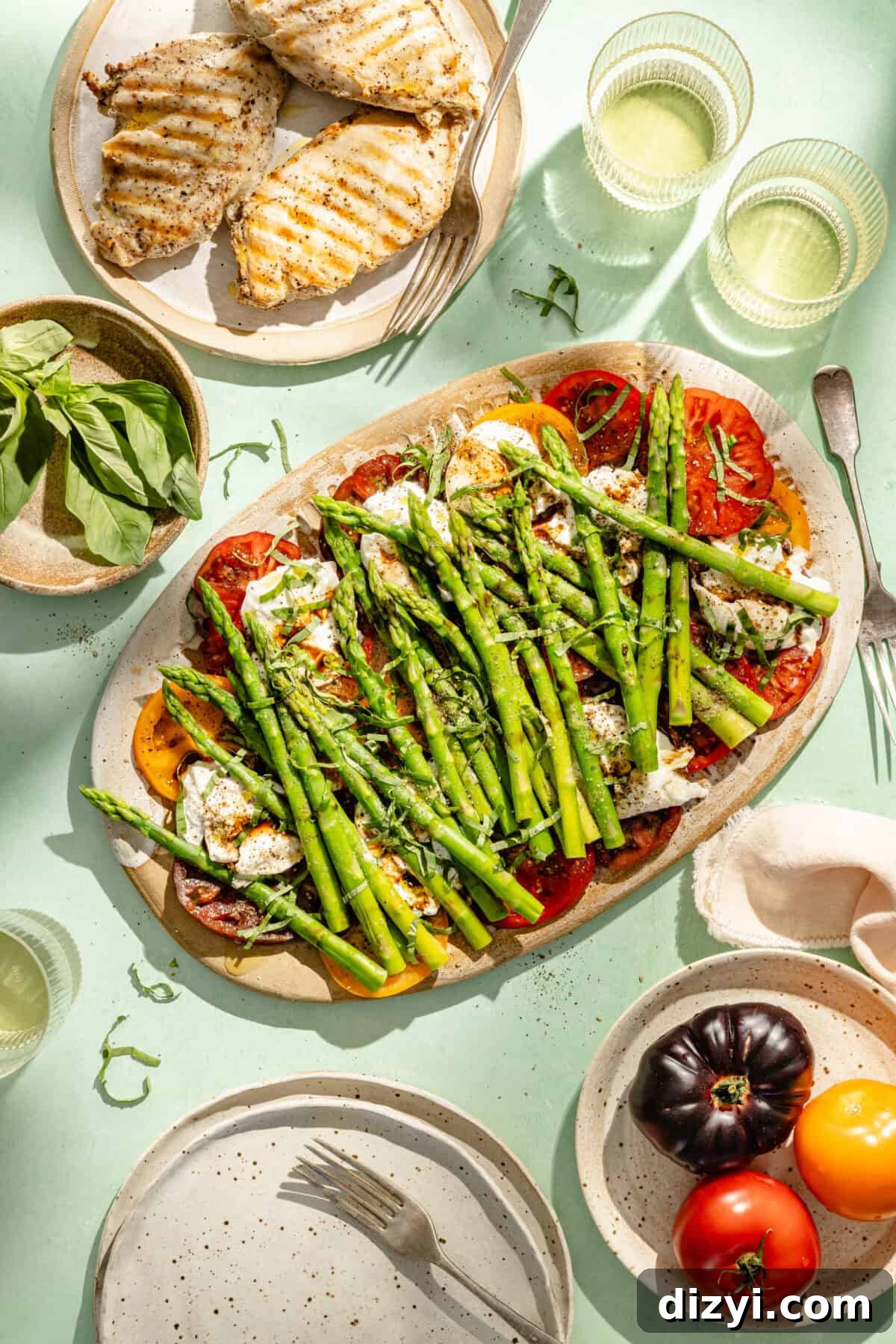 Burrata Caprese Salad with Asparagus and Tomatoes 2 a platter of caprese salad with asparagus on a light aqua background; a separate platter of grilled chicken breasts