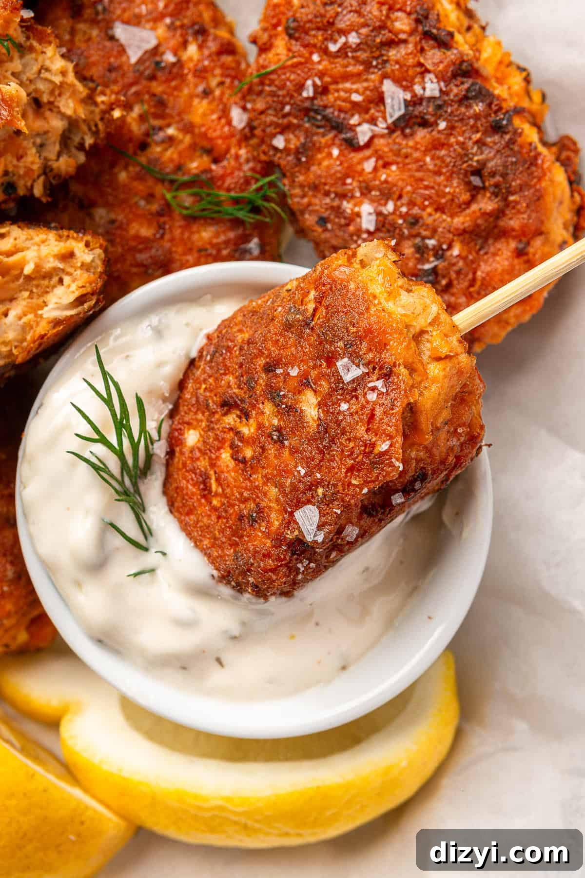 A finished salmon croquette on a skewer, being dipped into tartar sauce.