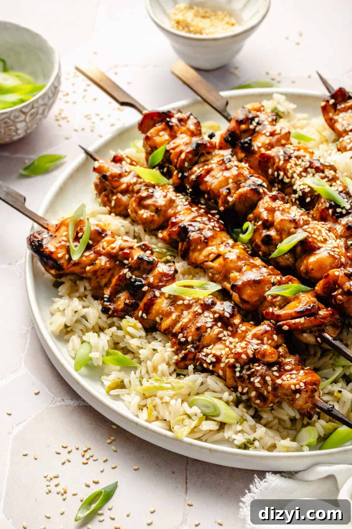 a close-up of grilled sesame chicken skewers over a bed of scallion rice