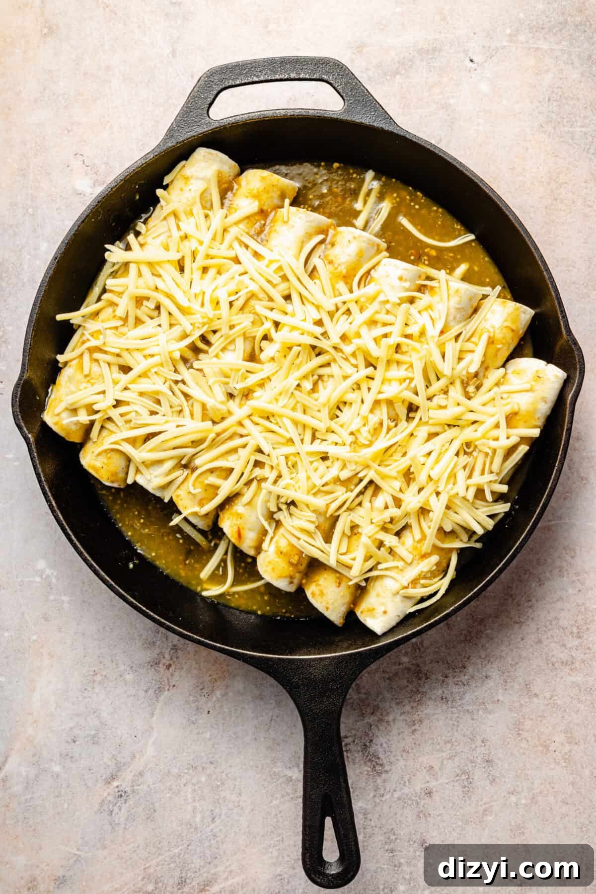 Creamy Green Chile Chicken Enchiladas 6 a cast-iron skillet with eight unbaked chicken enchiladas topped with cheese