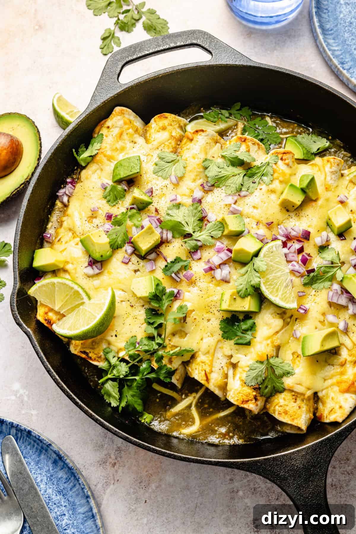 Creamy Green Chile Chicken Enchiladas 7 an up-close photo of chicken enchiladas topped with lime, avocado, cilantro, and red onion in a cast iron skillet