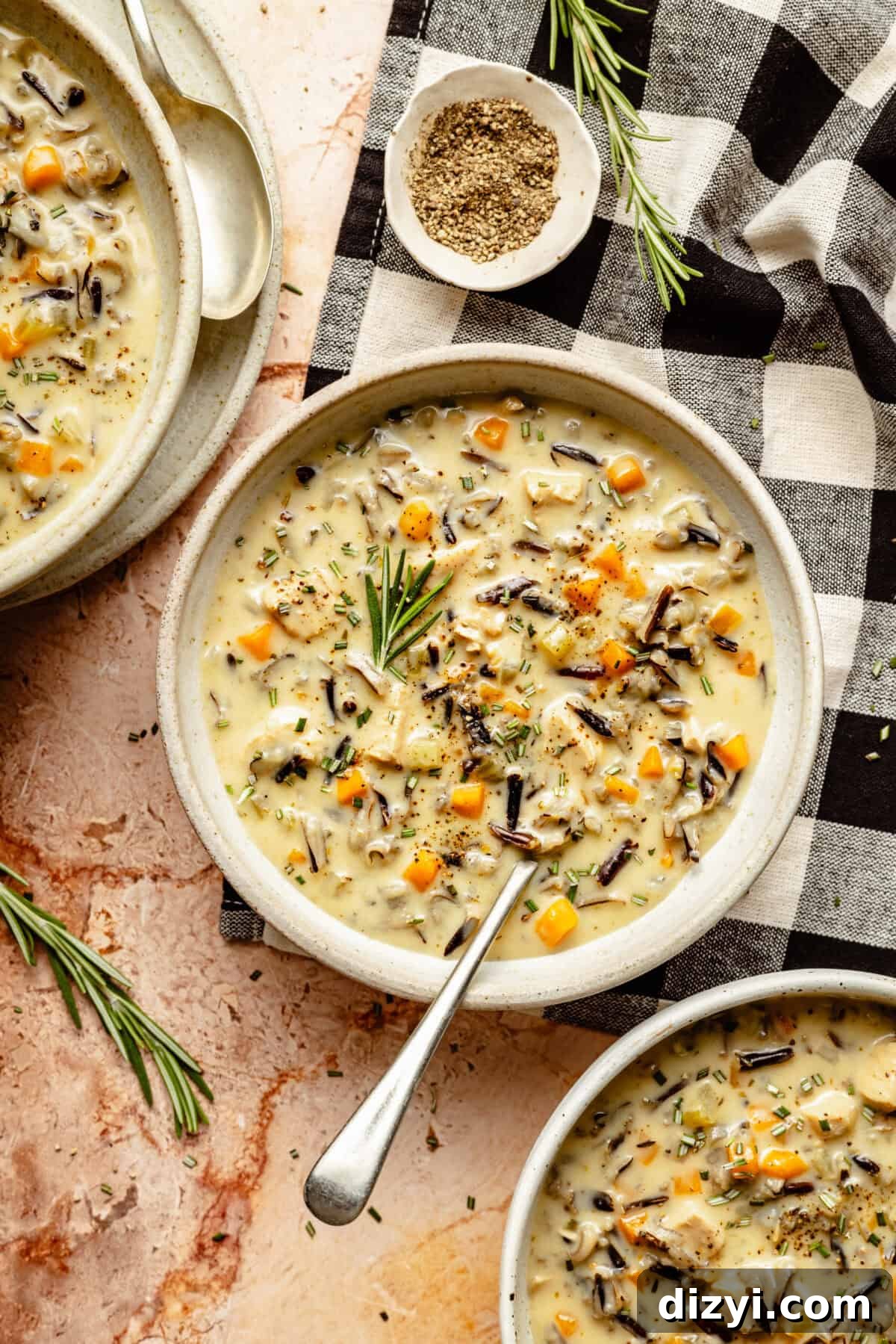 A finished bowl of Dairy Free Chicken and Wild Rice Soup on a table with a sprig of rosemary.
