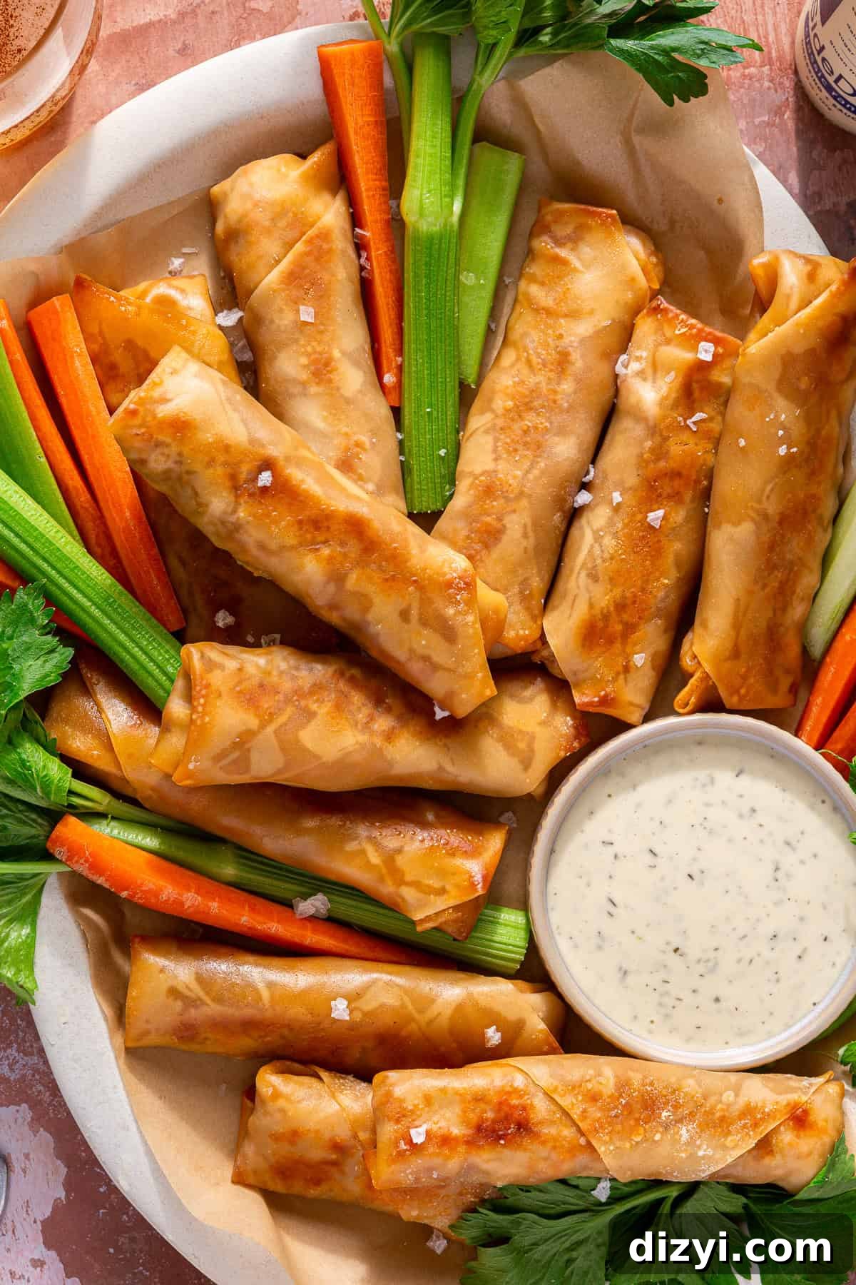 A finished platter of Buffalo Chicken Egg Rolls, served with carrots and celery, and a small silver dish of ranch.