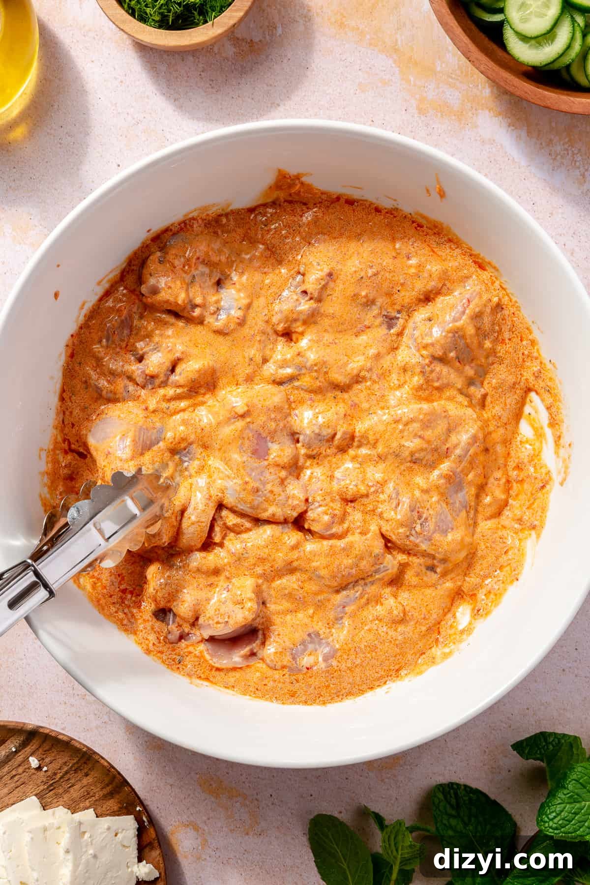 Raw chicken in harissa-yogurt marinade in large white bowl.