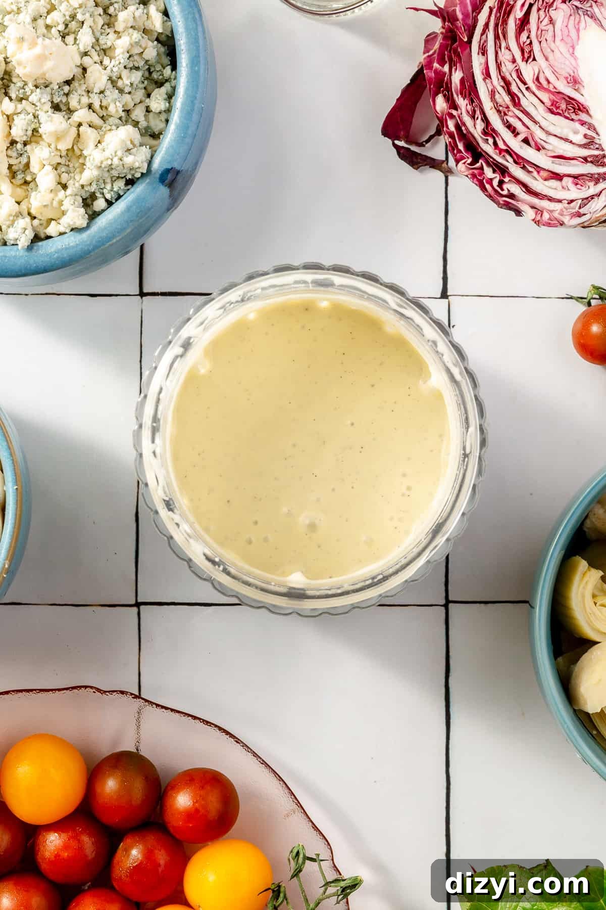 Gorgonzola dressing in a small glass bowl. Other Steakhouse Chopped Salad ingredients scatter around.