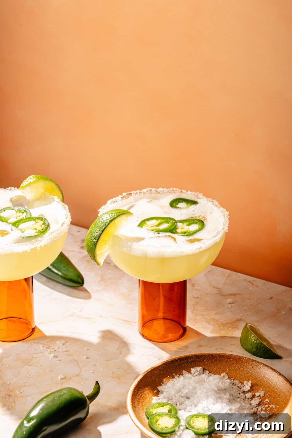 two glasses with spicy skinny margaritas garnished with lime, jalapeno peppers, and salt