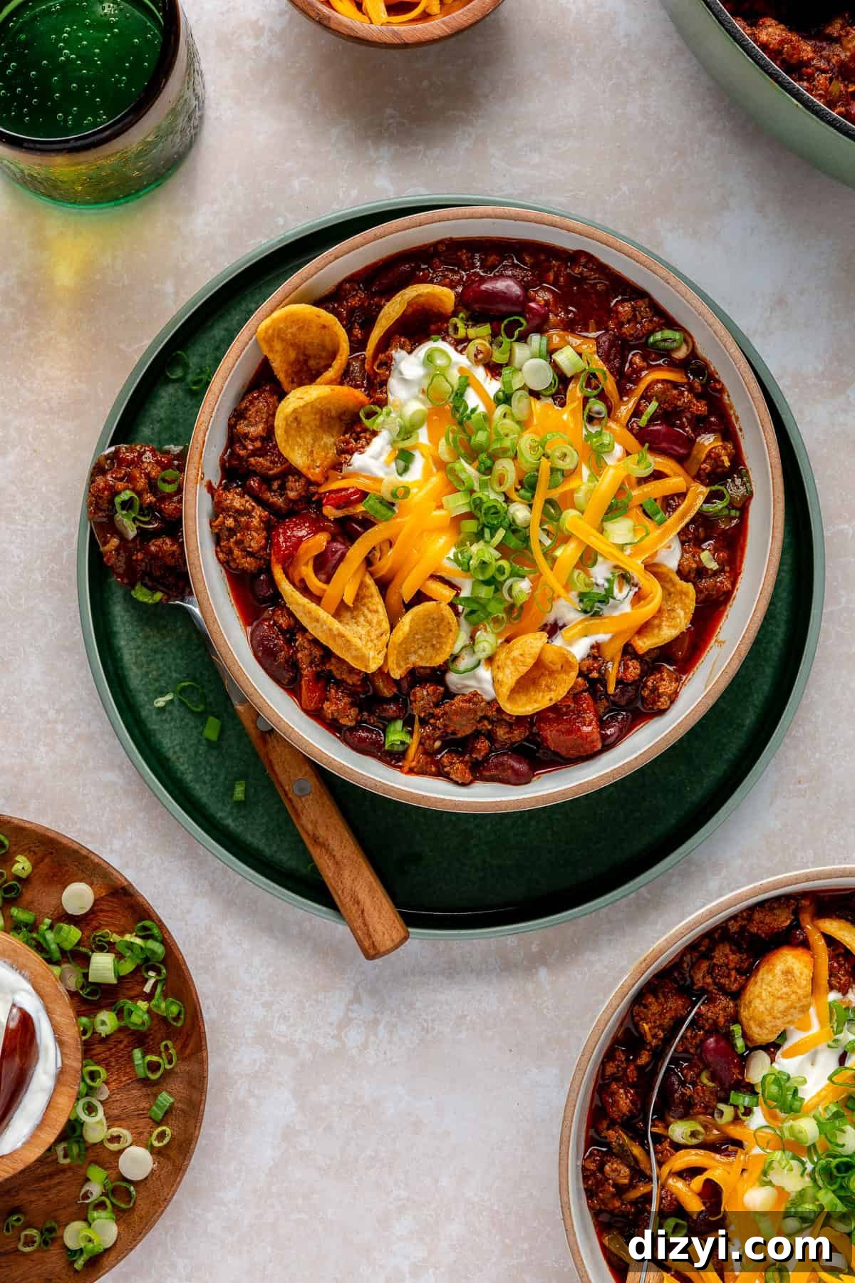 Green chargers with white bowls of Beef Chili with Beans on a white table.