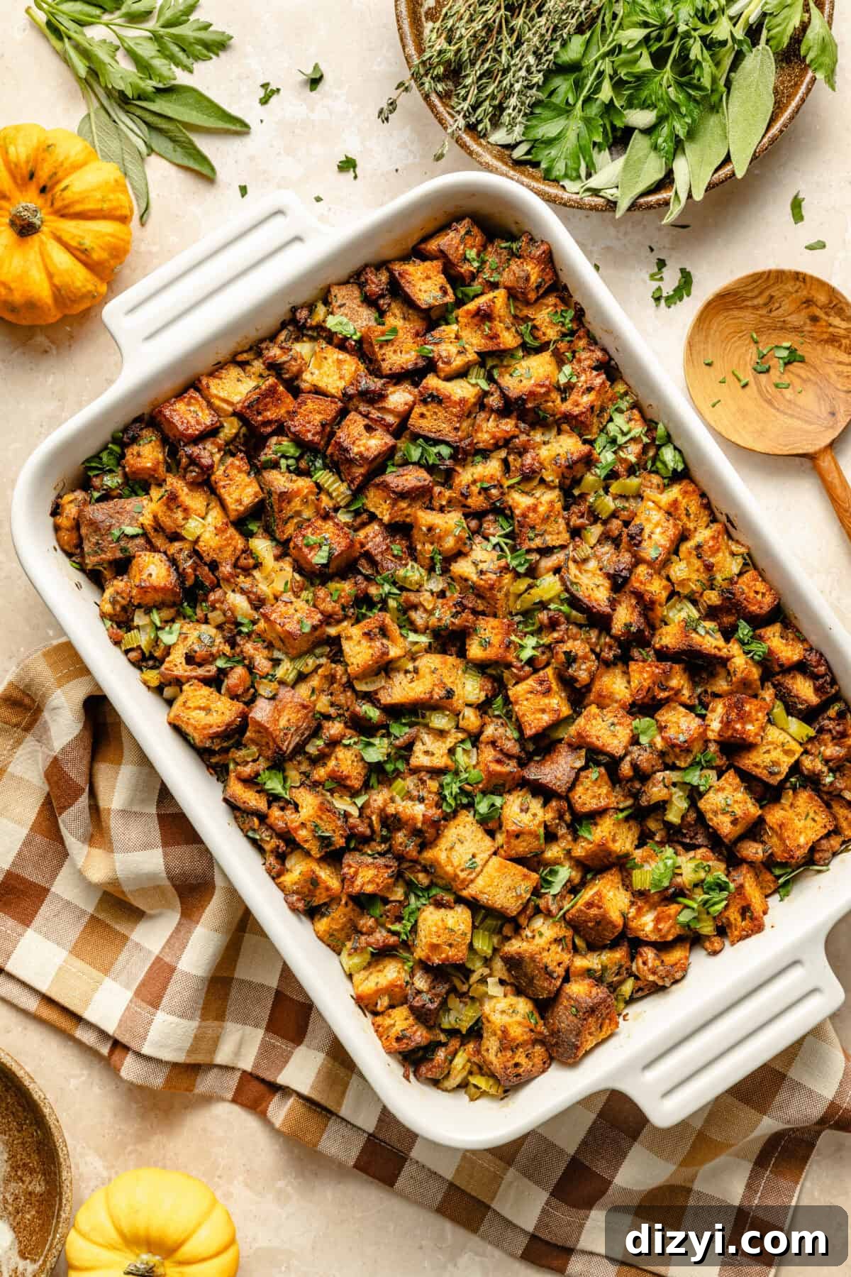 Oven-Baked Sausage and Sage Stuffing 2 a large white baking dish filled with cooked stuffing featuring bread cubes, sausage, and fresh herbs with a brown gingham napkin