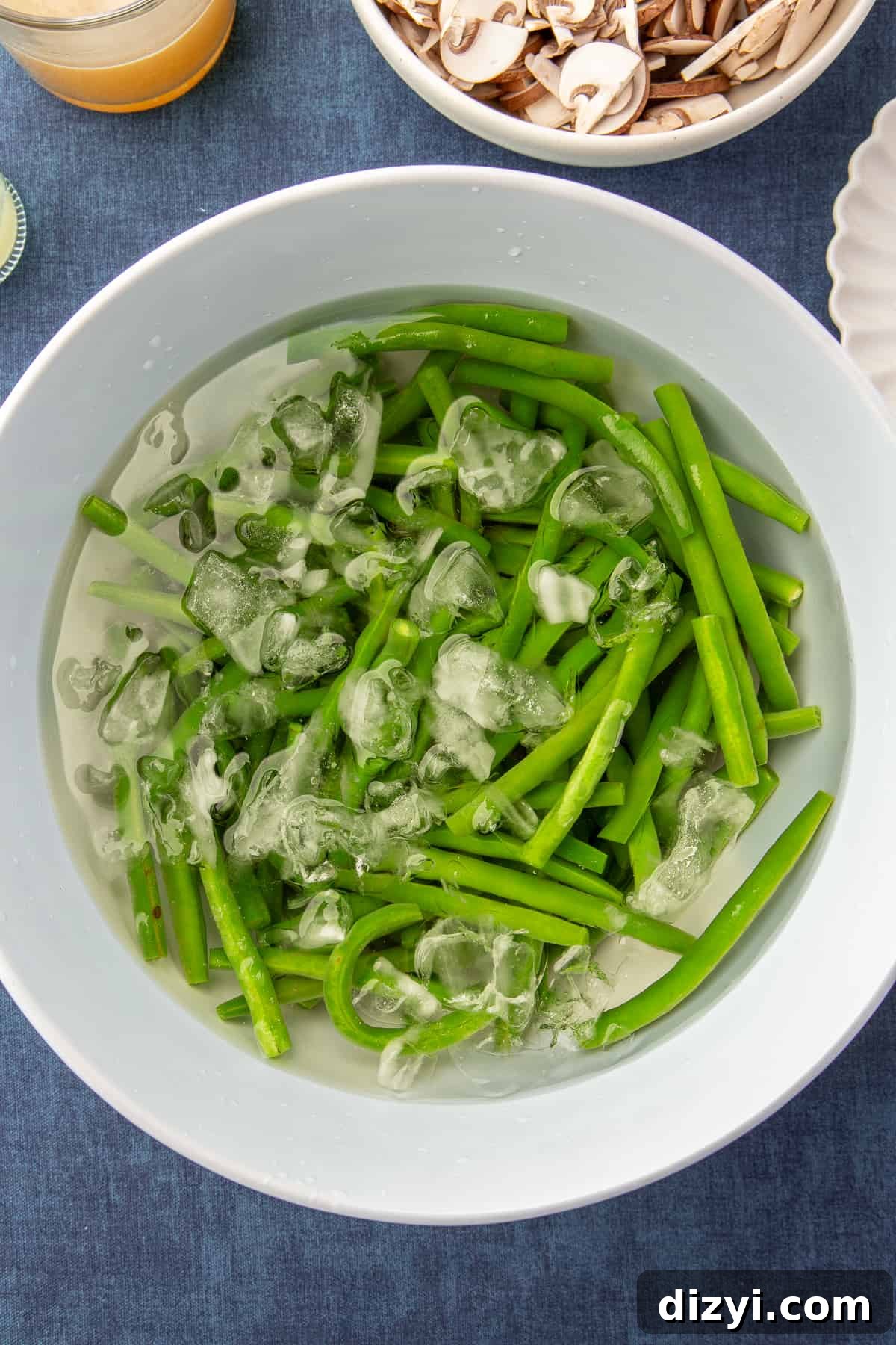 Par-cooked green beans in an ice bath in a large white bowl