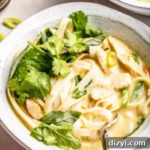 Chicken noodle soup in small white stoneware bowl and topped with lots of herbs.