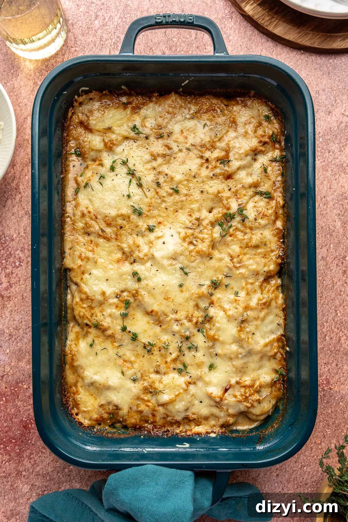 Creamy Scalloped Potatoes with Caramelized Onions 2 Blue baking dish of Caramelized Onion Scalloped Potatoes on red backdrop.