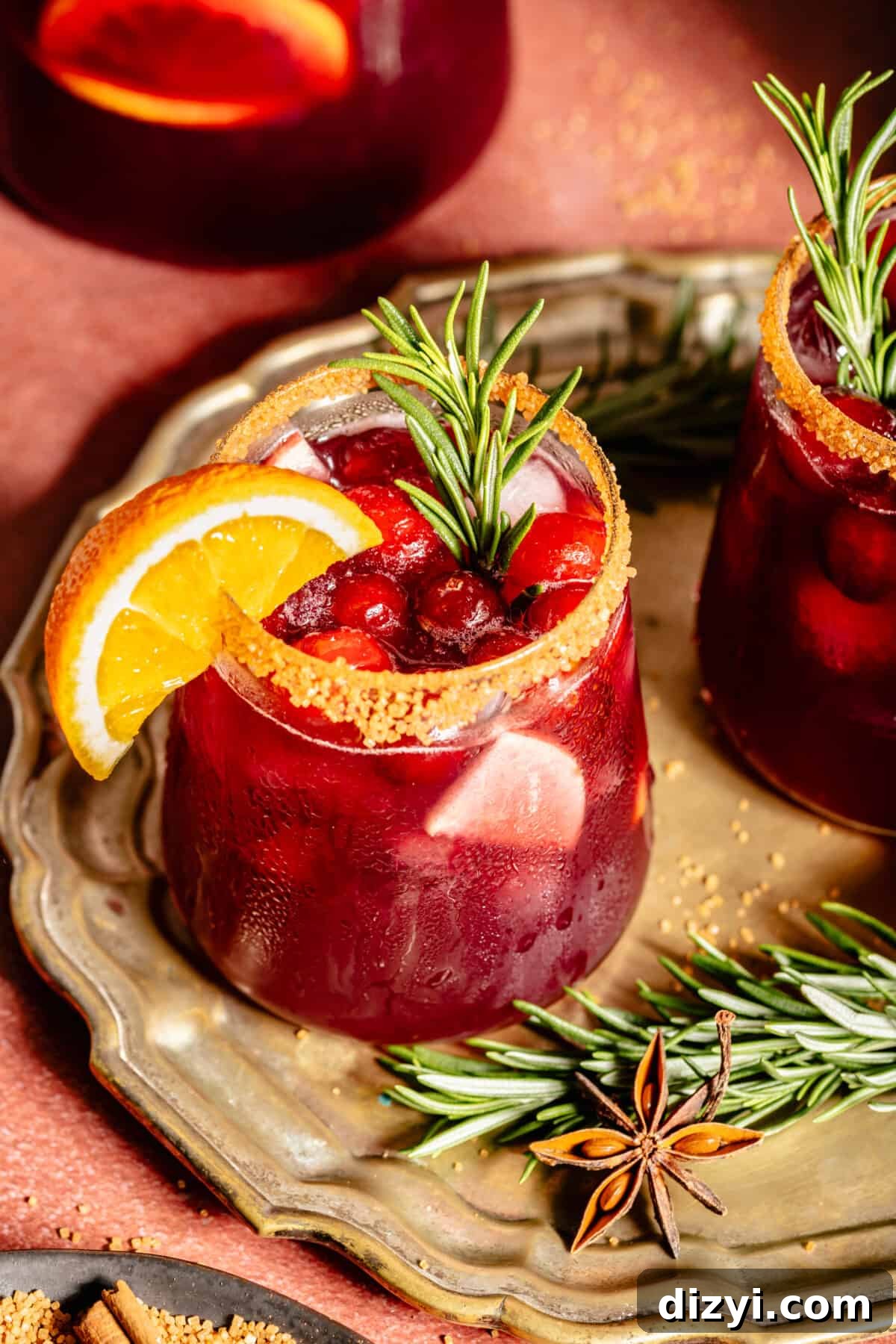 Glass of Holiday Sangria. Orange slice on rim. Sprig of rosemary in glass.