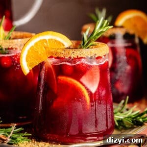 Glass of Holiday Sangria. Orange slice on rim. Sprig of rosemary in glass.