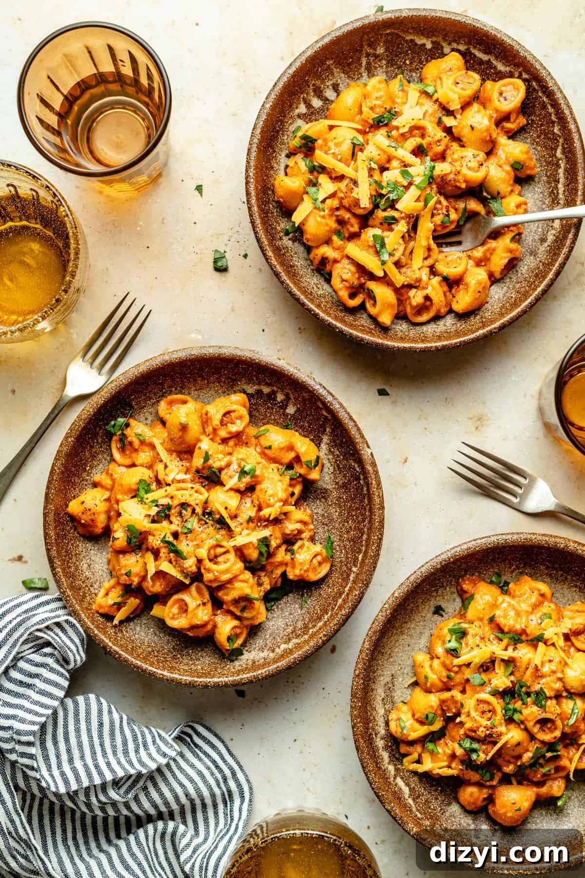 Three plates filled with cooked pasta with forks surrounded by cups and napkins.