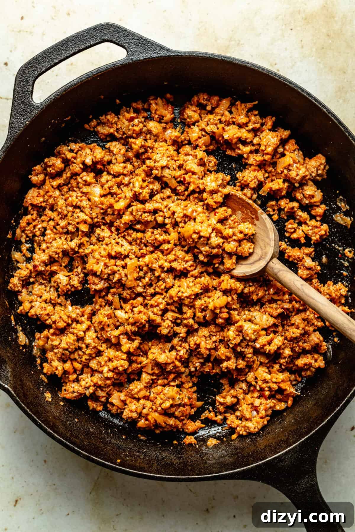 Cooked ground beef in black cast iron skillet with spoon in it.