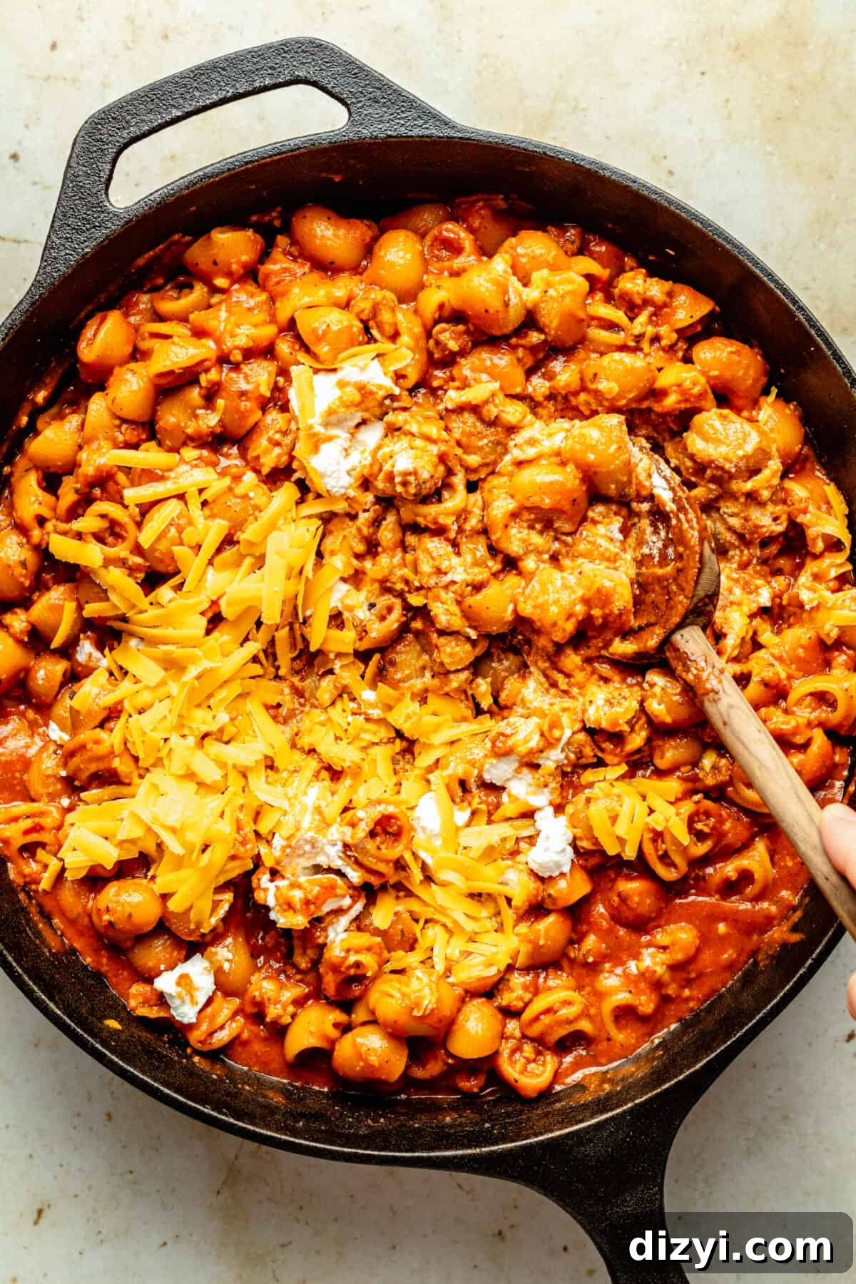 Cook ground beef, pasta, and red sauce in cast iron skillet with cheese being stirred in with spoon.