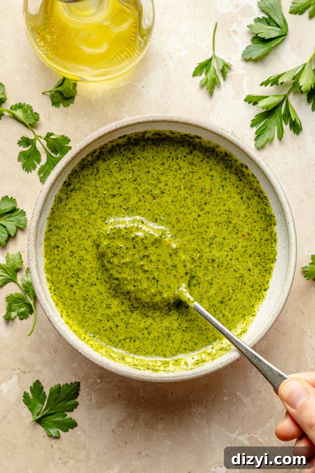 Bowl of Chimichurri Dressing on neutral background that has scattered cilantro on it.