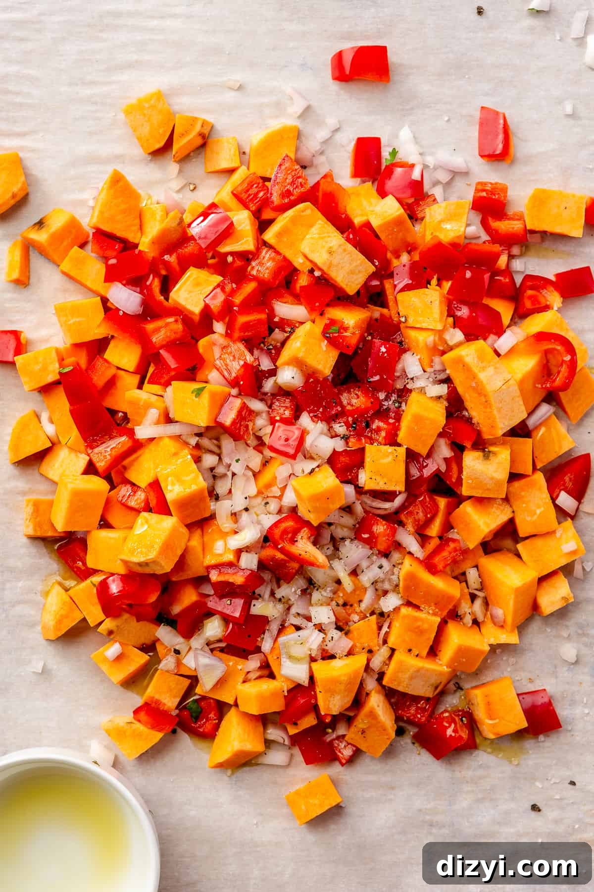Diced sweet potato, bell peppers, and shallot piled on a parchment-lined sheet pan.