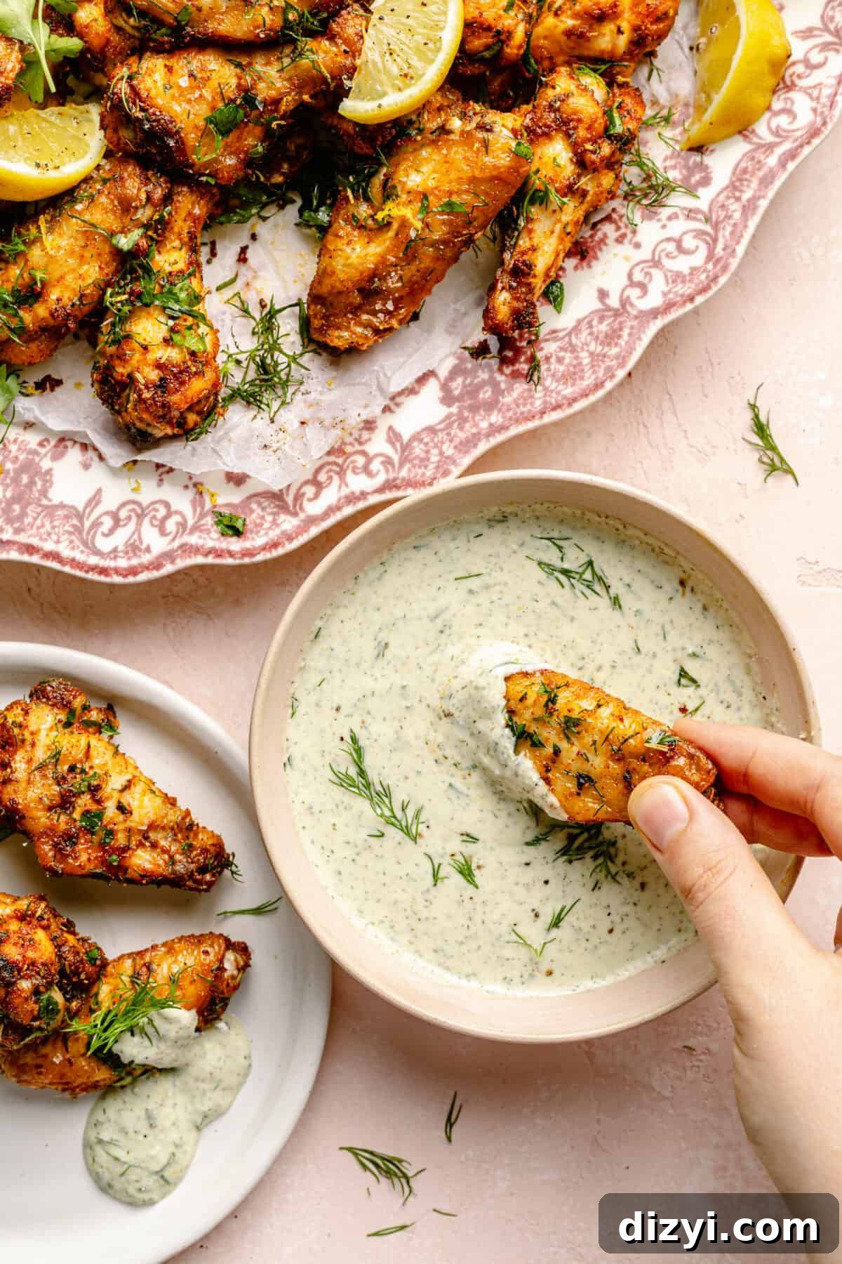 Greek-Inspired Chicken Wing being dipped into feta sauce. Platter of wings in background.