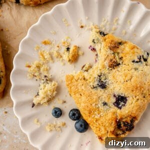 One scone on plate with bite taken out of it and crumbs.