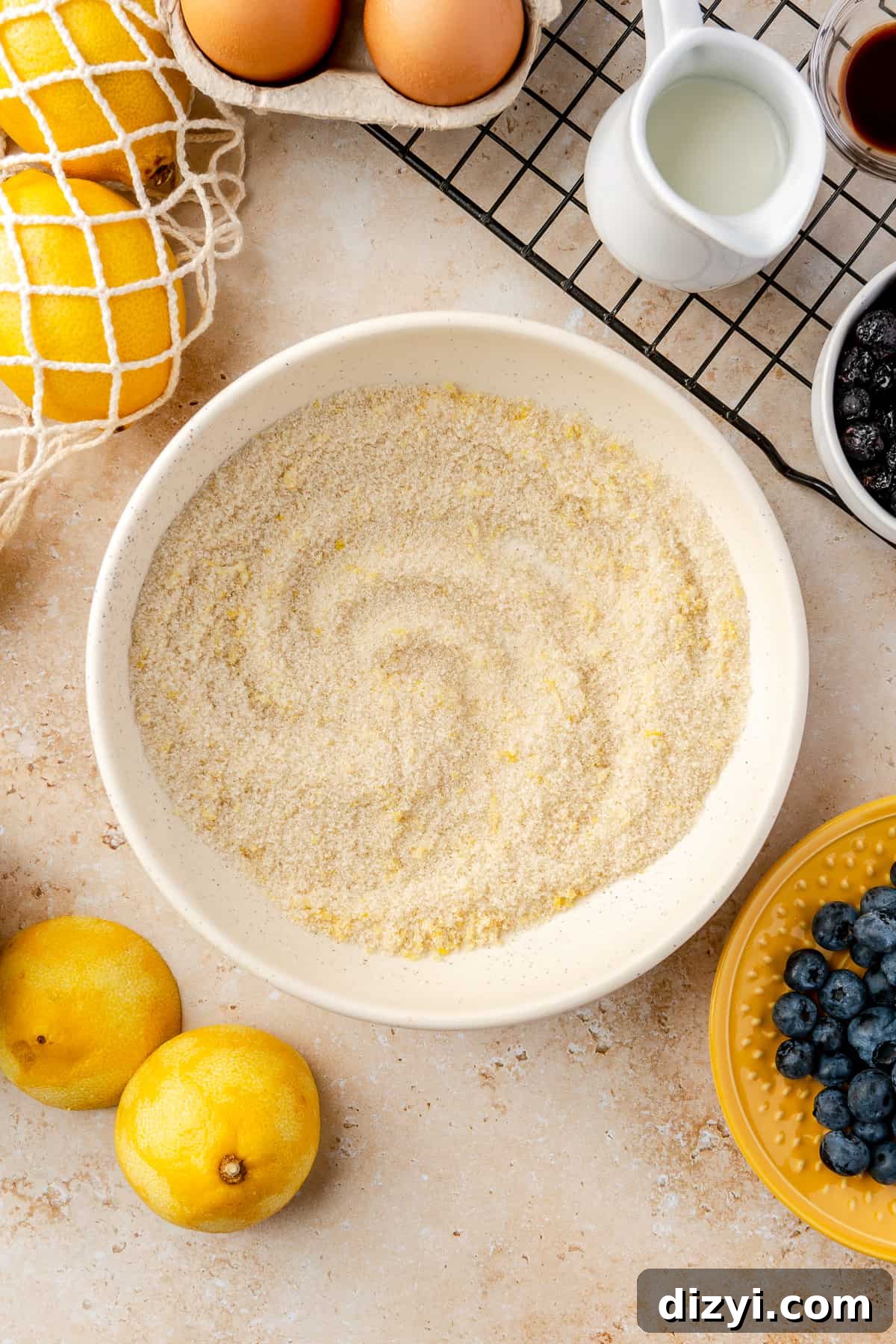 Lemon zest and sugar combined in a small bowl. Other scone ingredients scatter around the bowl.