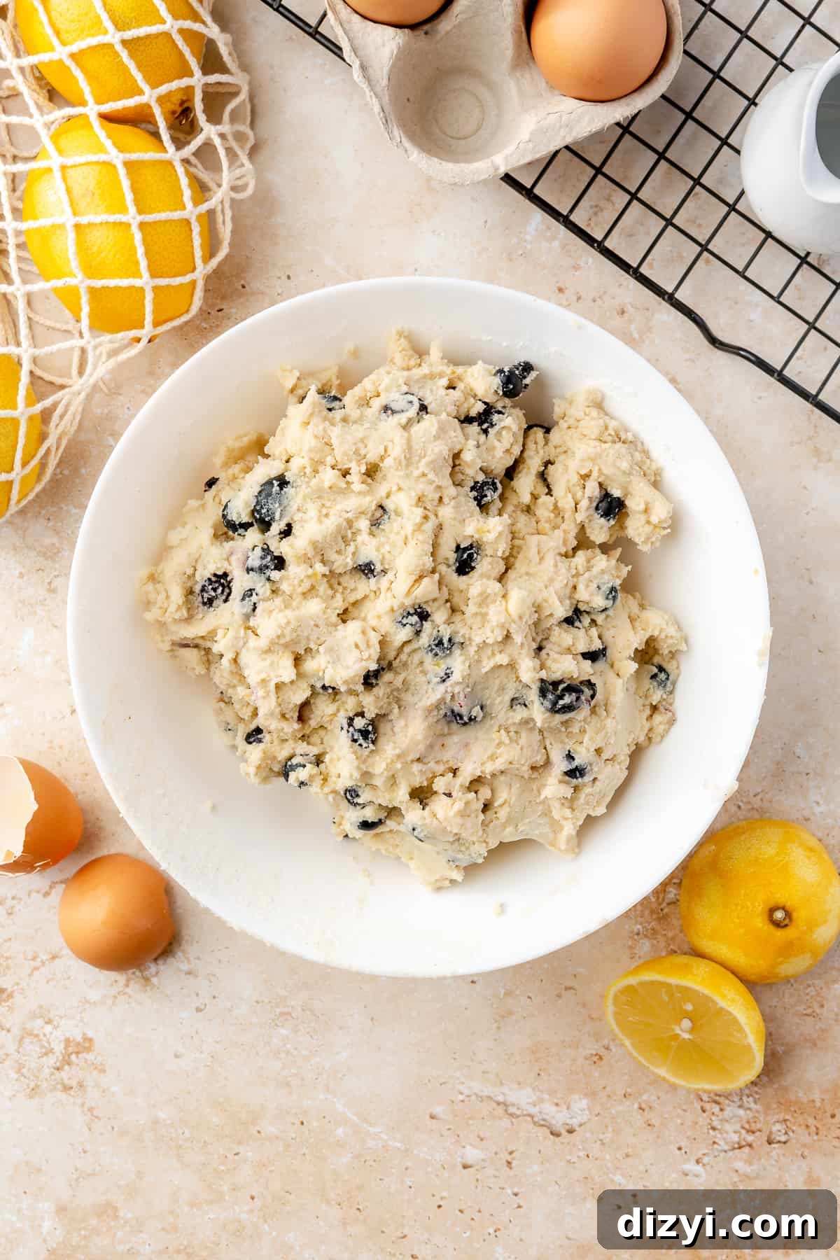 Final scone dough in large bowl on neutral background. Scattered ingredients around the bowl.
