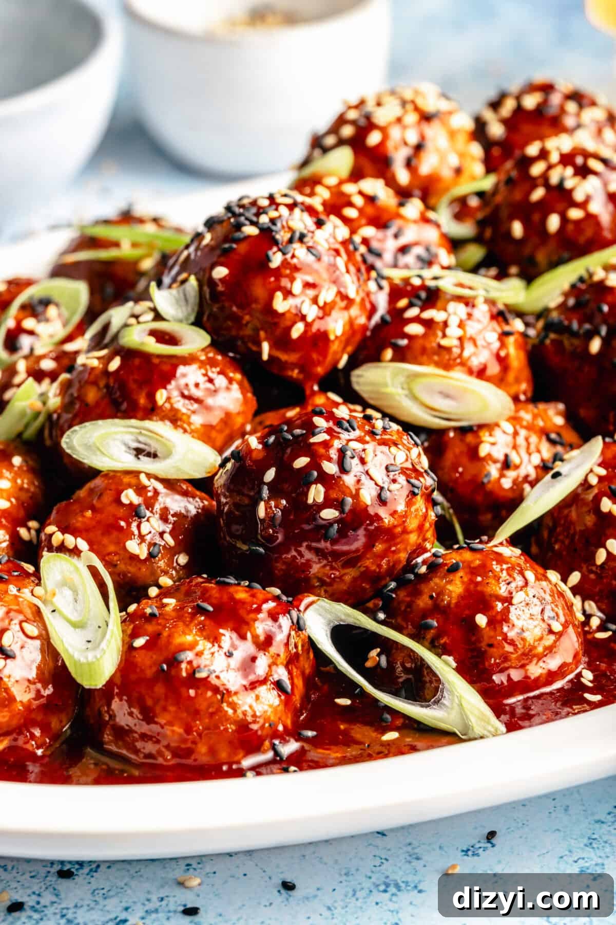 Close up of Korean-Inspired BBQ Chicken Meatballs on white platter. Meatballs garnished with sesame seeds and green onions.