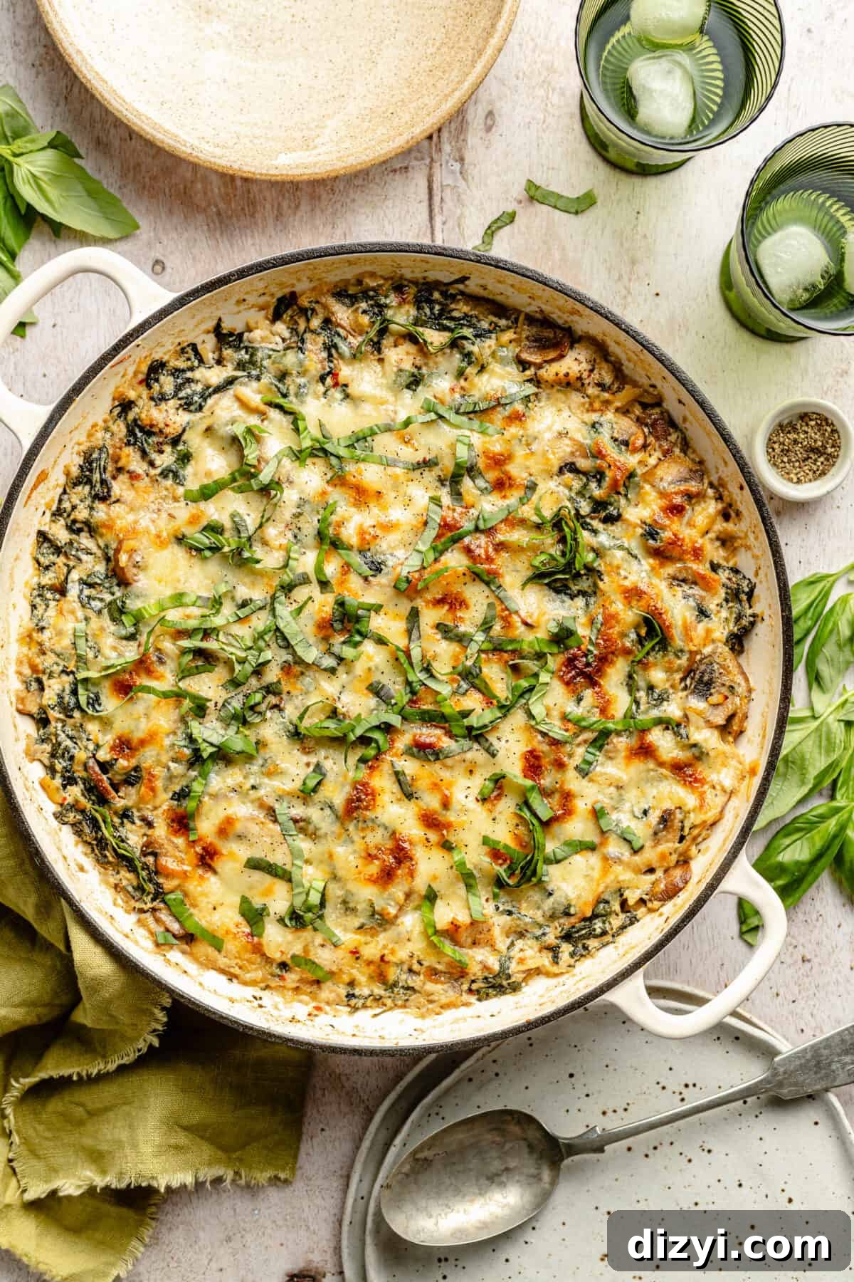 Creamy Ricotta Chicken and Orzo Skillet in white skillet with cups, plates and utensils scatter around it.