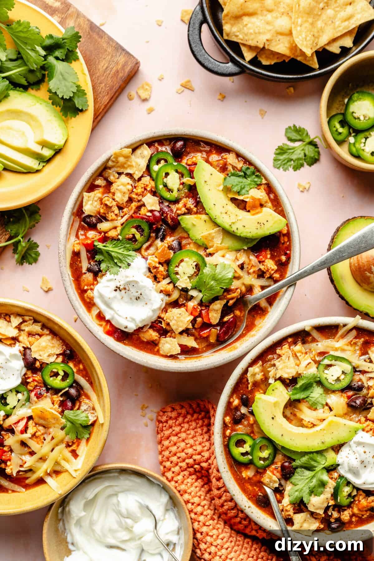 Cheesy Chicken Enchilada Chili Recipe 2 Three bowls of Chicken Enchilada Chili with garnishes surrounding.