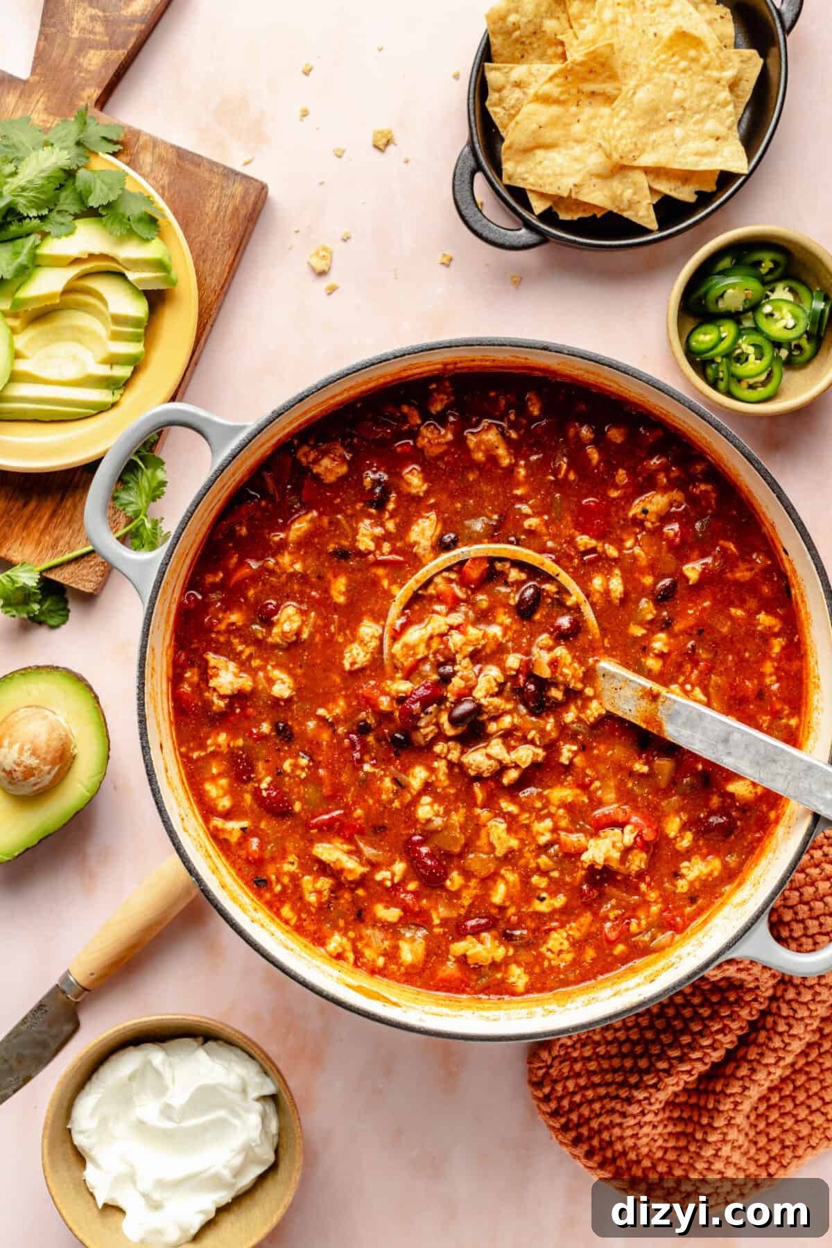 Cheesy Chicken Enchilada Chili Recipe 3 Large pot of Chicken Enchilada Chili with ladle in it. Garnishes scattered around.