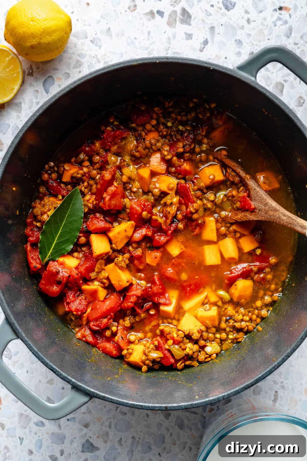 Pot of veggies, lentils, broth, and canned tomatoes. Bay leaf resting on top.