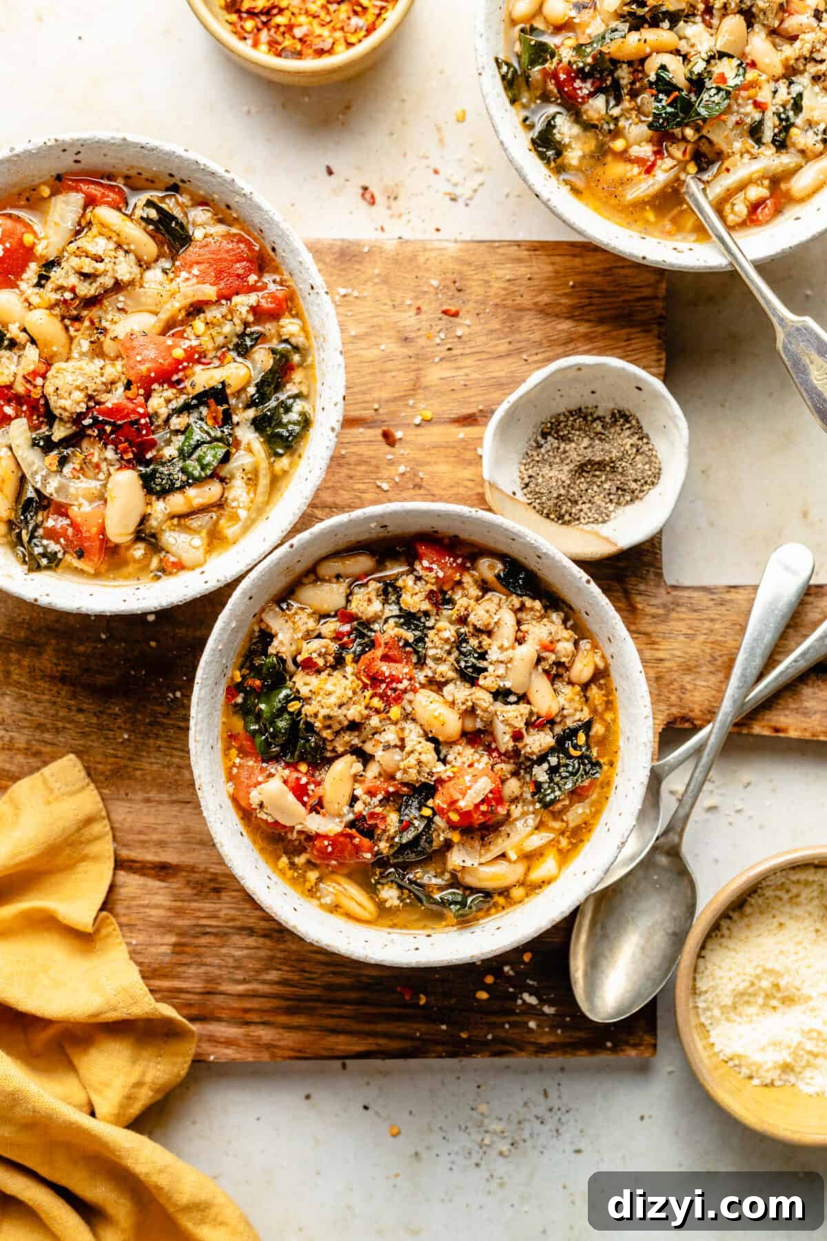Bowls of Sausage, Fennel, and White Bean Soup on wood serving board. Bowls of garnishes scattered around.