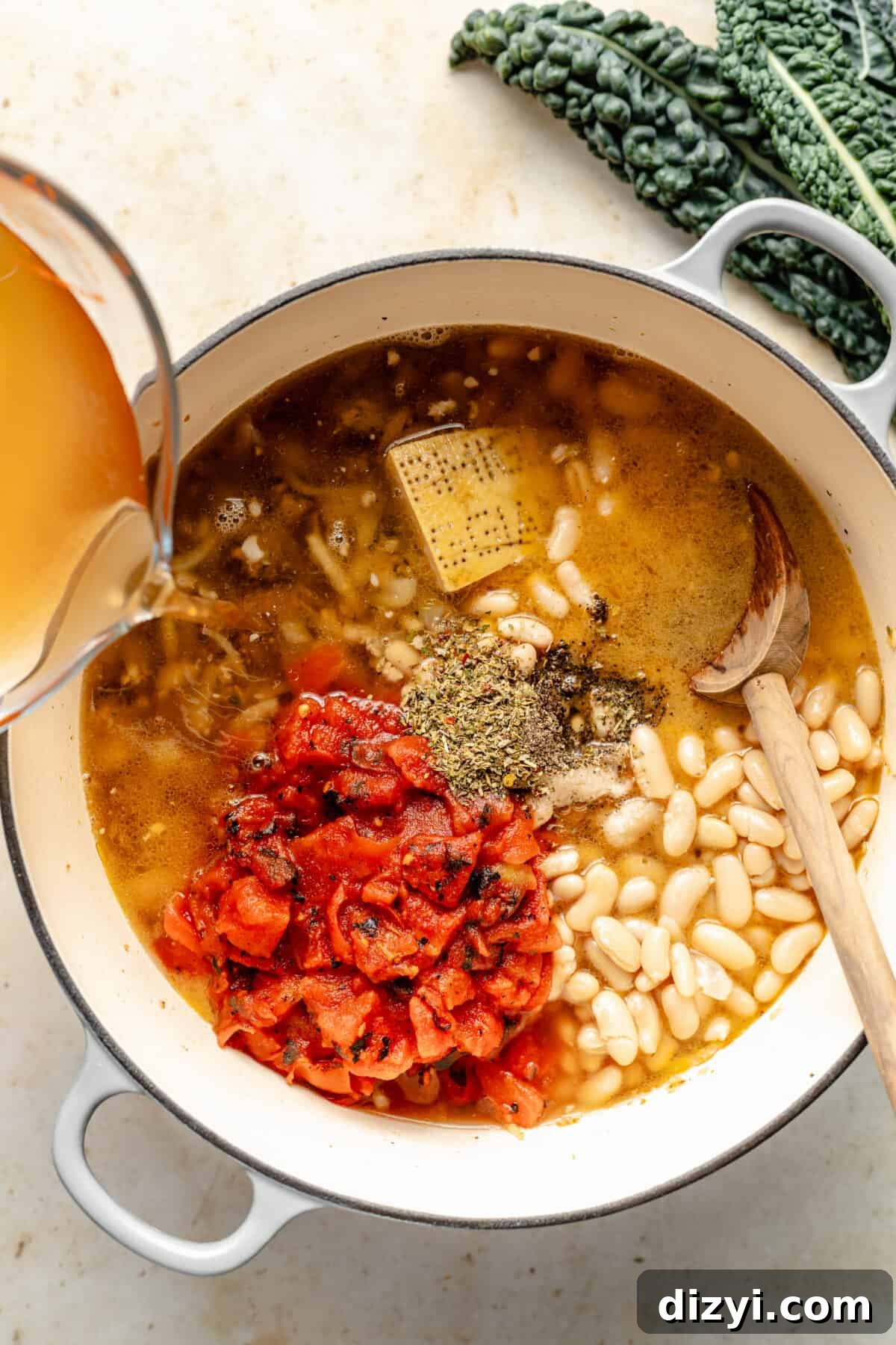 White dutch oven filled with beans, broth, tomatoes, seasoning, and cheese rind.