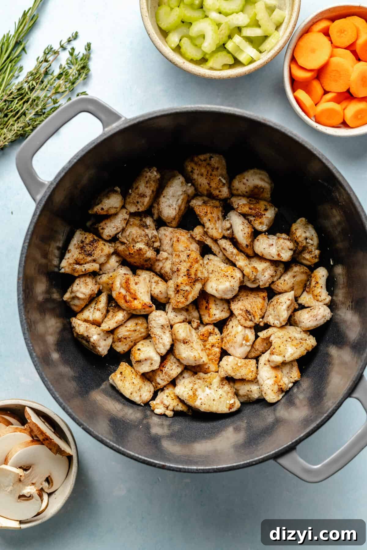 Classic Chicken Stew Recipe with Tender Vegetables 4 Cut chicken browned in large, dark dutch oven.. Bowls of celery and carrots in the corner of the photo.
