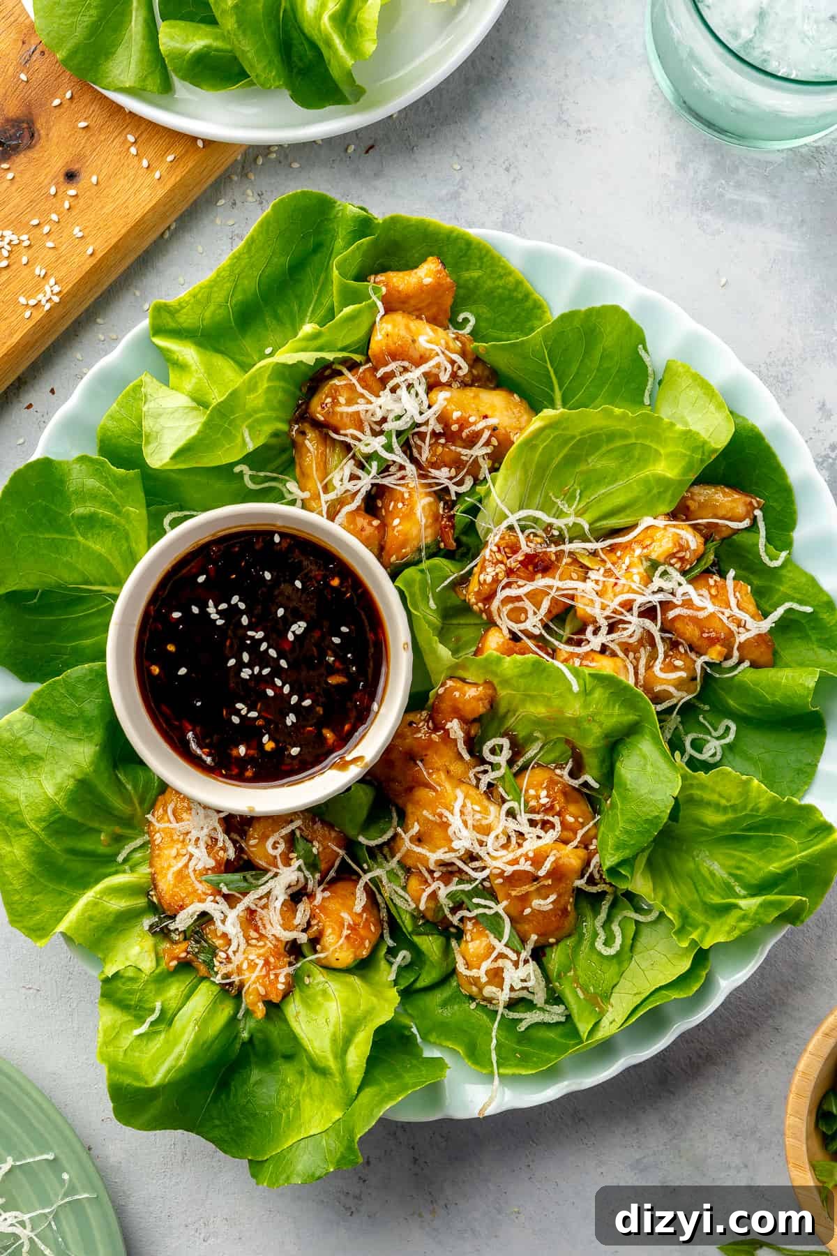 How to Make Honey Garlic Chicken Lettuce Wraps 2 Four Honey-Garlic Chicken Lettuce Wraps on a round plate with a small bowl of extra sauce.