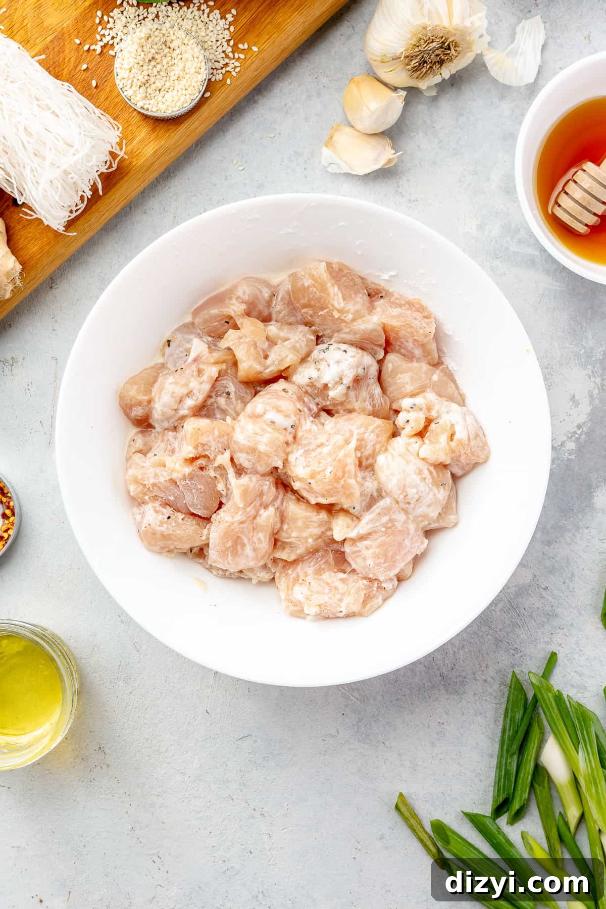 How to Make Honey Garlic Chicken Lettuce Wraps 4 White bowl filled of marinating chicken with other ingredients scattered around it.