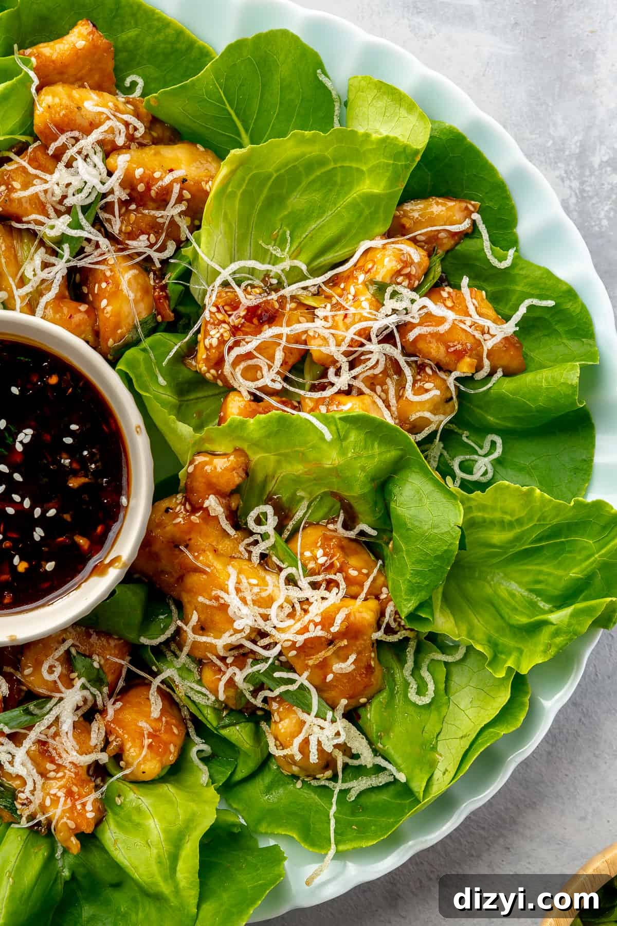 How to Make Honey Garlic Chicken Lettuce Wraps 9 Close up of Four Honey Sesame Chicken Lettuce Cups on a round plate with a small bowl of extra sauce.