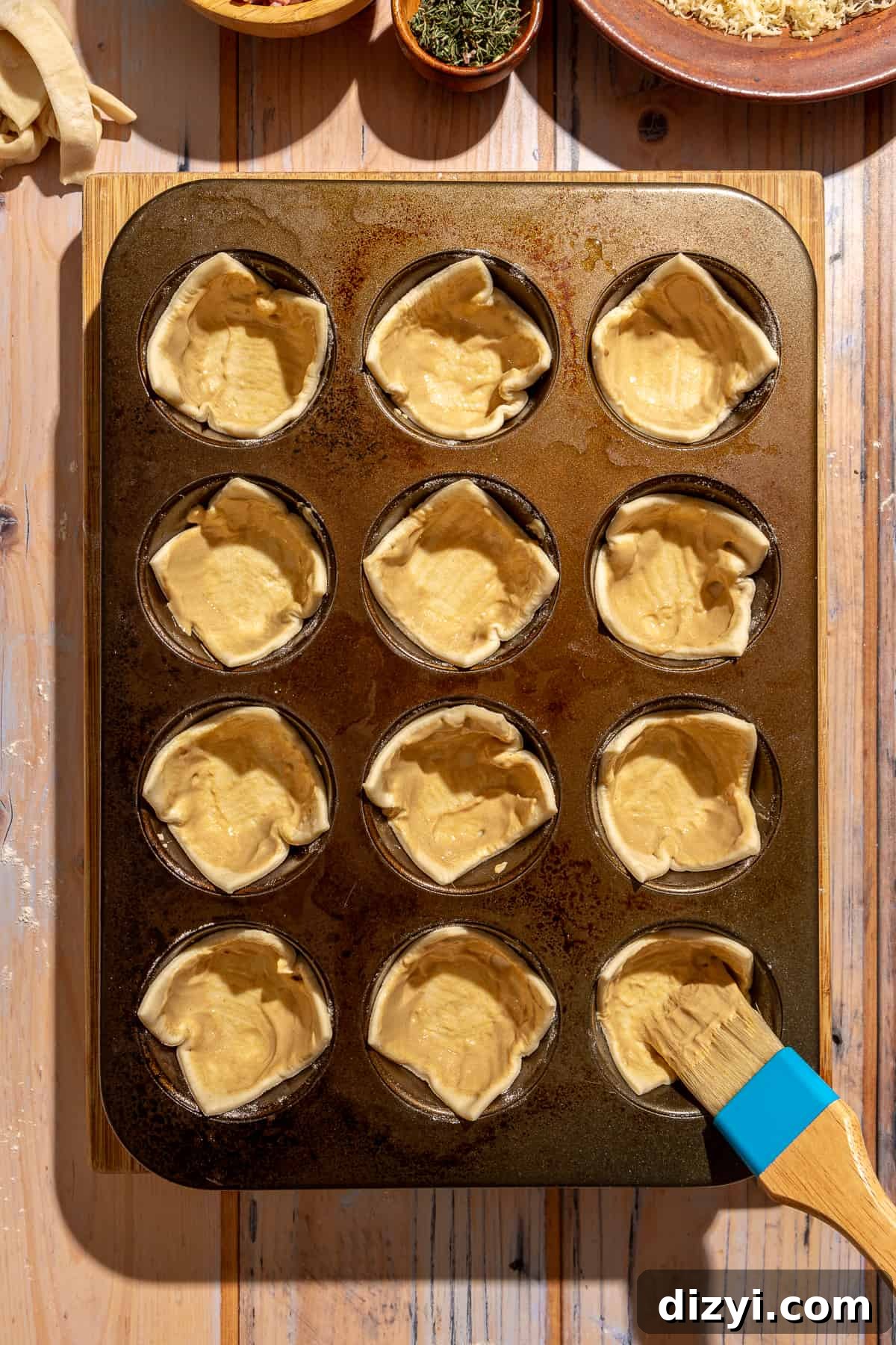 Puff pastry in muffin tin openings. Pastry brush with Dijon mustard being brushed onto puff pastry.