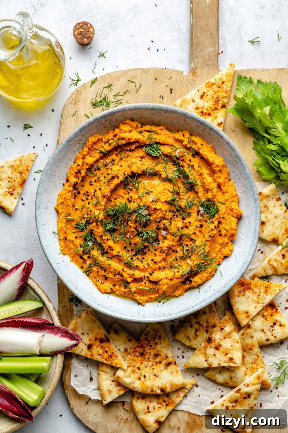 Small bowl of Harissa Carrot Dip with pita and veggies surrounding it.