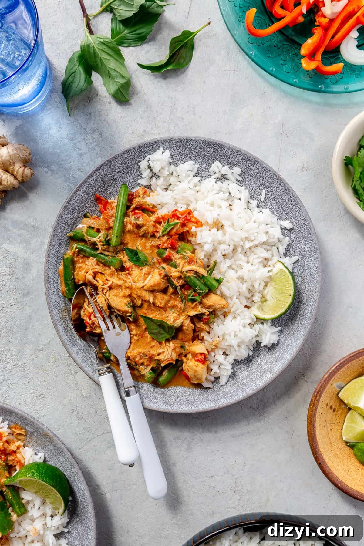 Slow Cooker Thai Red Curry with Chicken and Vegetables 7 Blue bowl filled with Slow Cooker Thai Red Curry Chicken and Veggies and rice. Cup of water and bowls of garnishes surrounding.