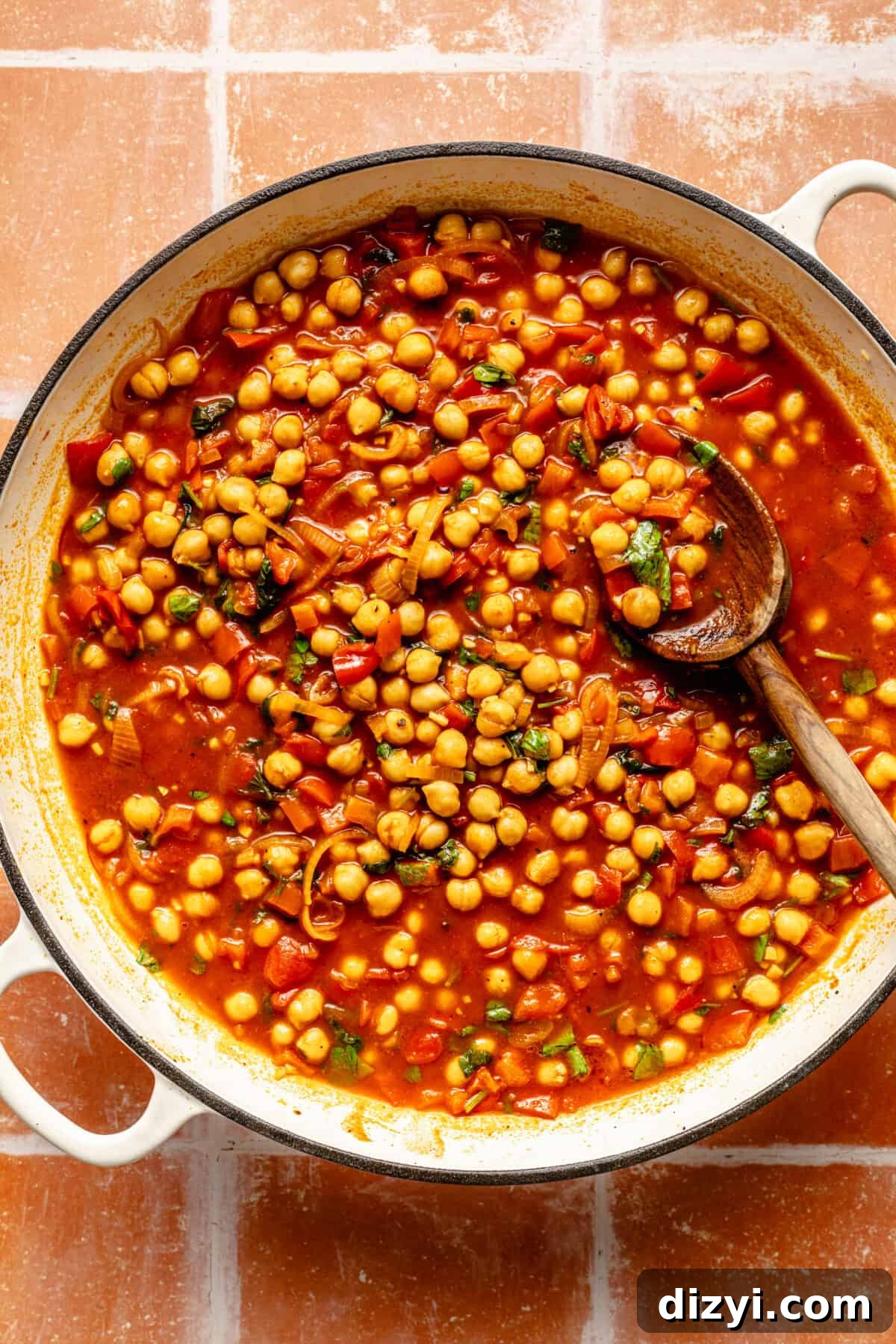 Chickpeas simmering in broth in a white skillet.