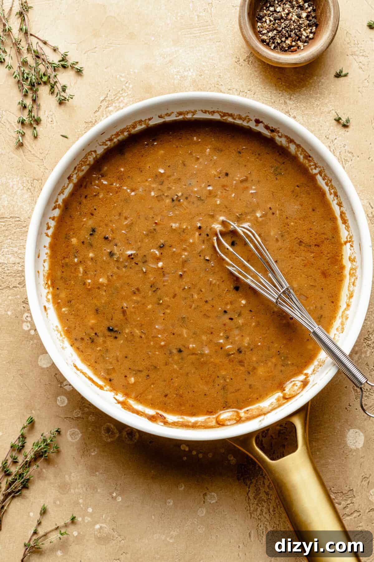 Au Poivre sauce in a skillet. Whisk resting in sauce. Herbs scattered around skillet.