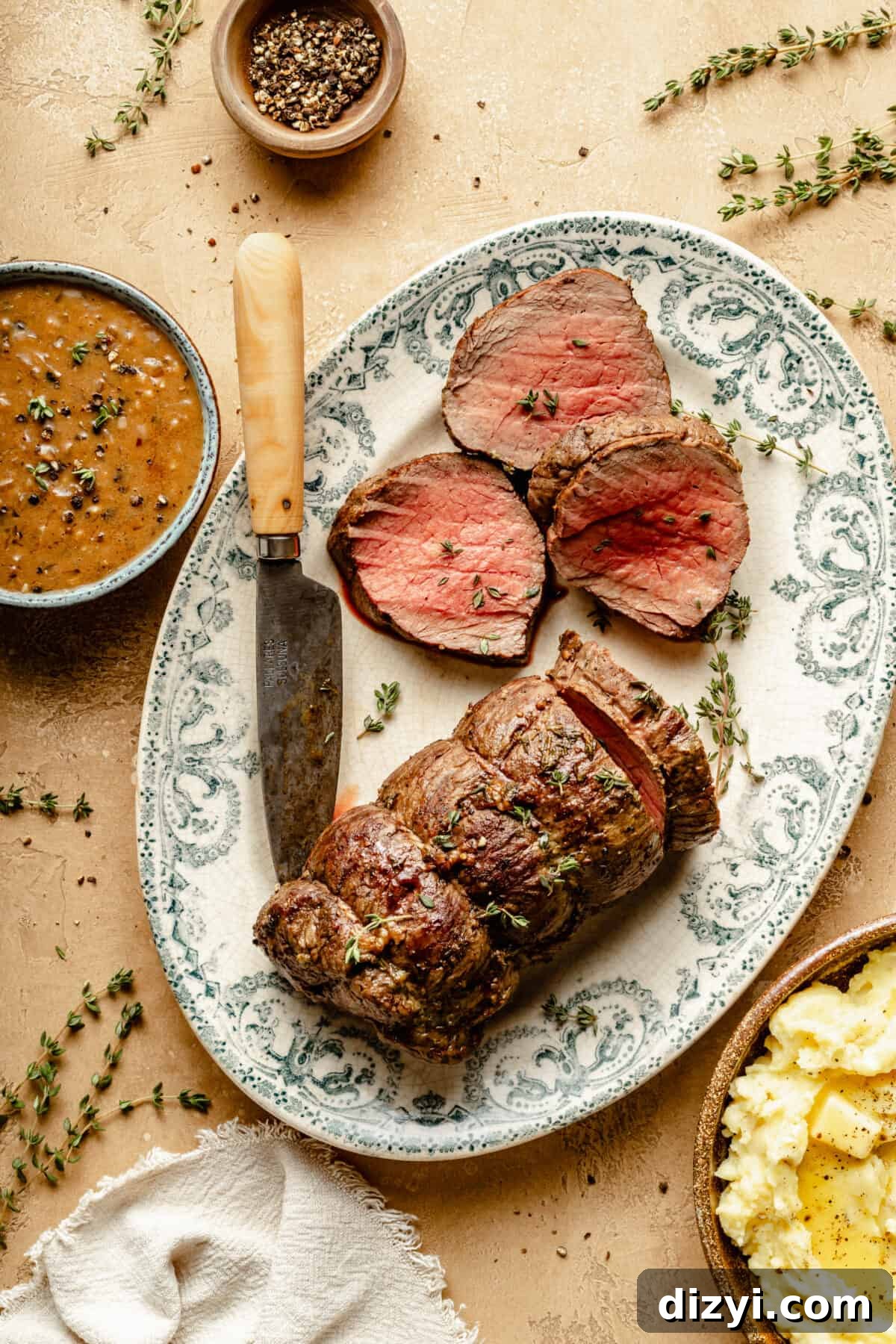 Beef Tenderloin partially sliced on platter. Knife resting on platter. Small bowl of Au Poivre next to platter.