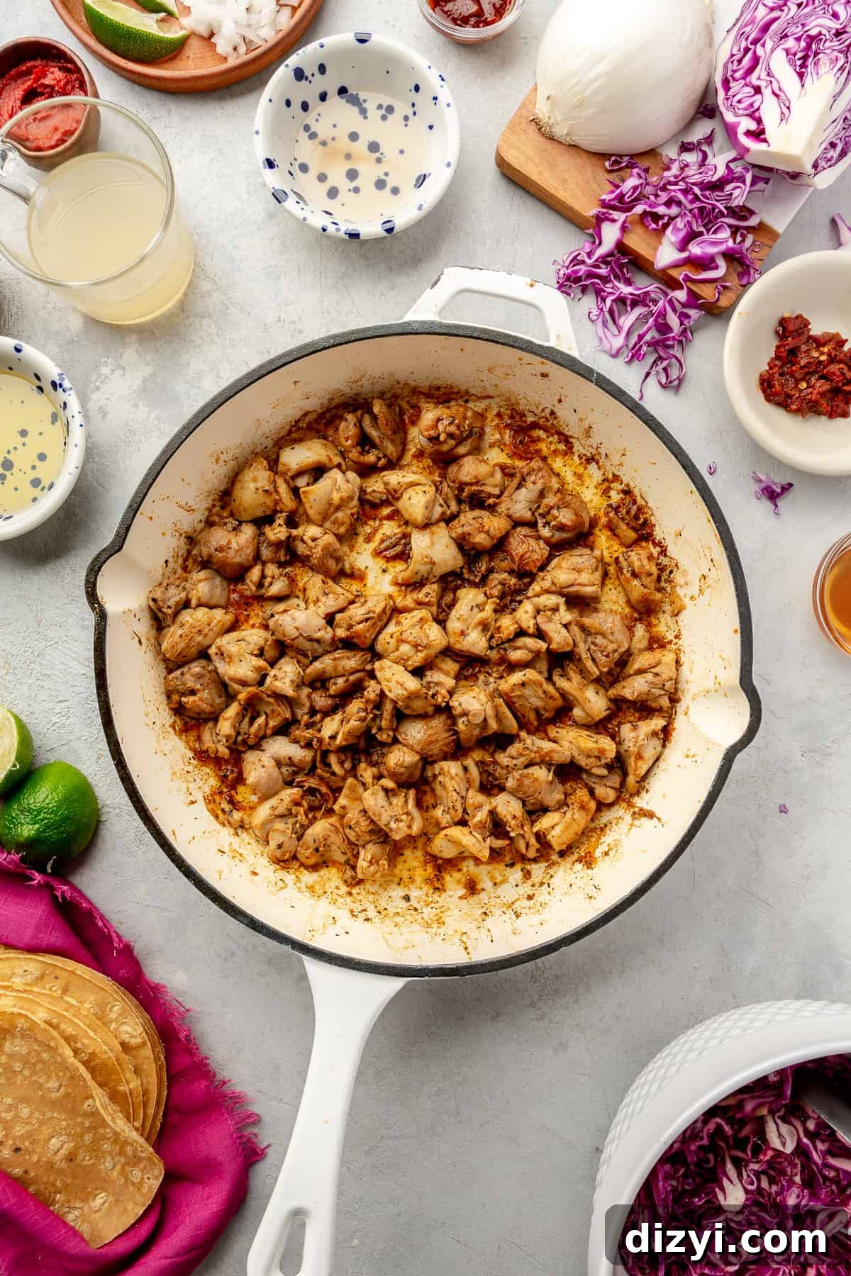 Seasoned chicken in skillet. Taco ingredients scattered around.