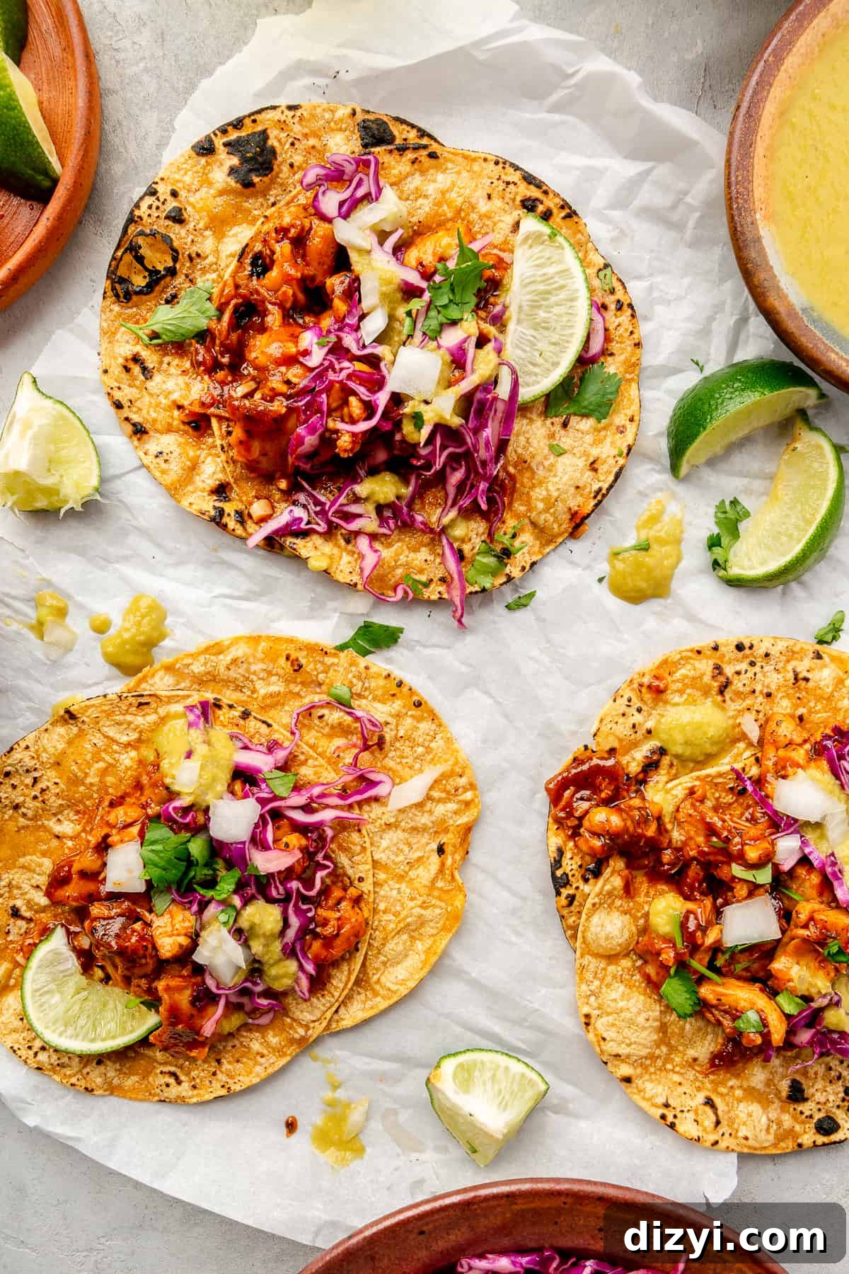 Three Saucy Chipotle Chicken Tacos on parchment paper. Lime wedges scattered around.
