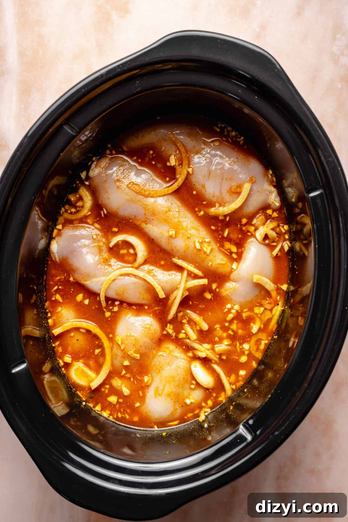 Slow cooker filed with tagine ingredients and raw chicken in it.