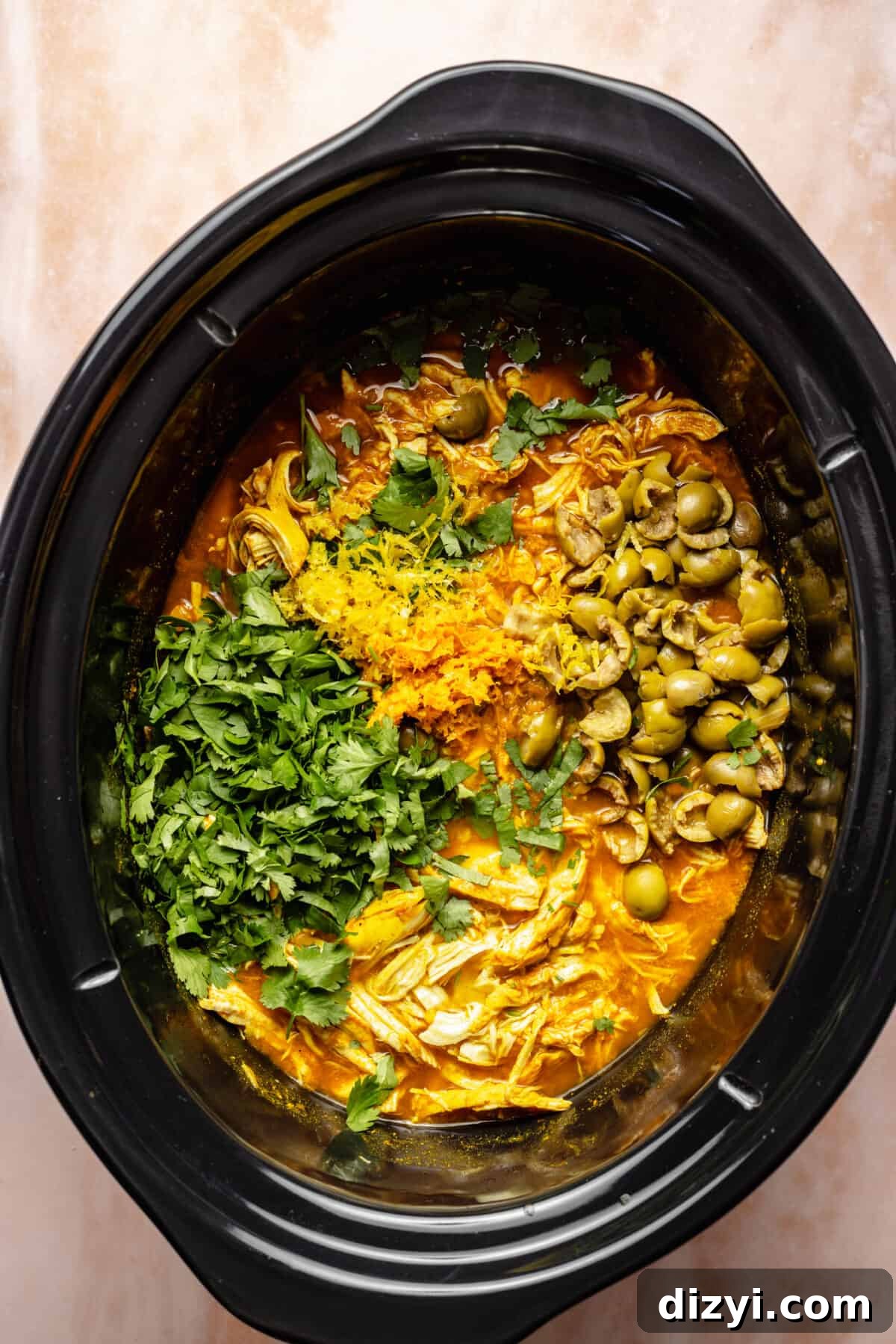 Shredded chicken in crockpot with additional ingredients on top.