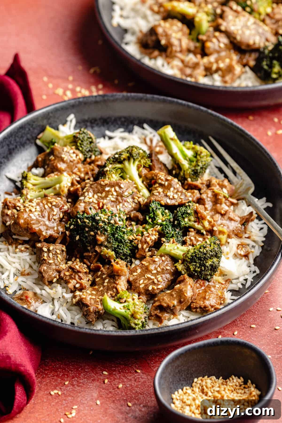 Slow Cooker Beef and Broccoli in bowls on red backdrop.