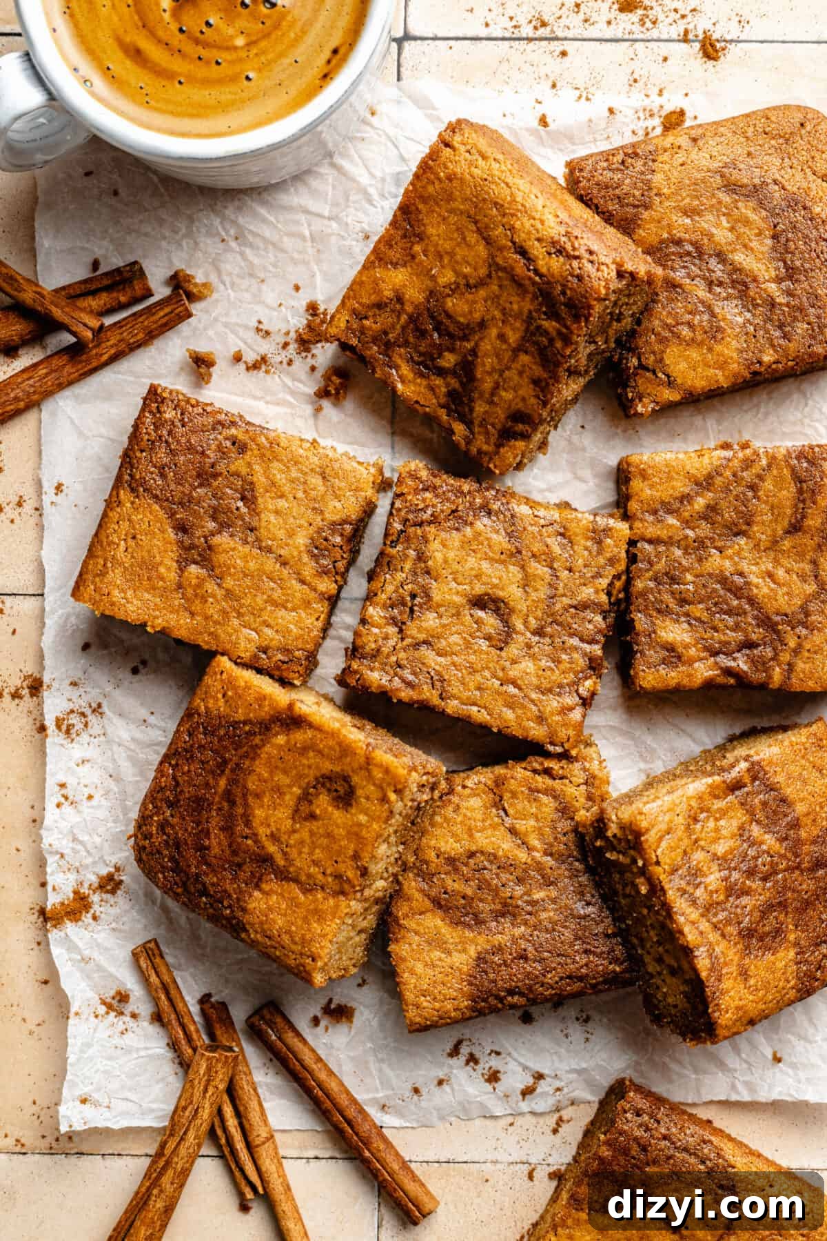 Paleo Cinnamon Swirl Cake sliced on parchment paper. Cinnamon sticks and cup of coffee peaking in.