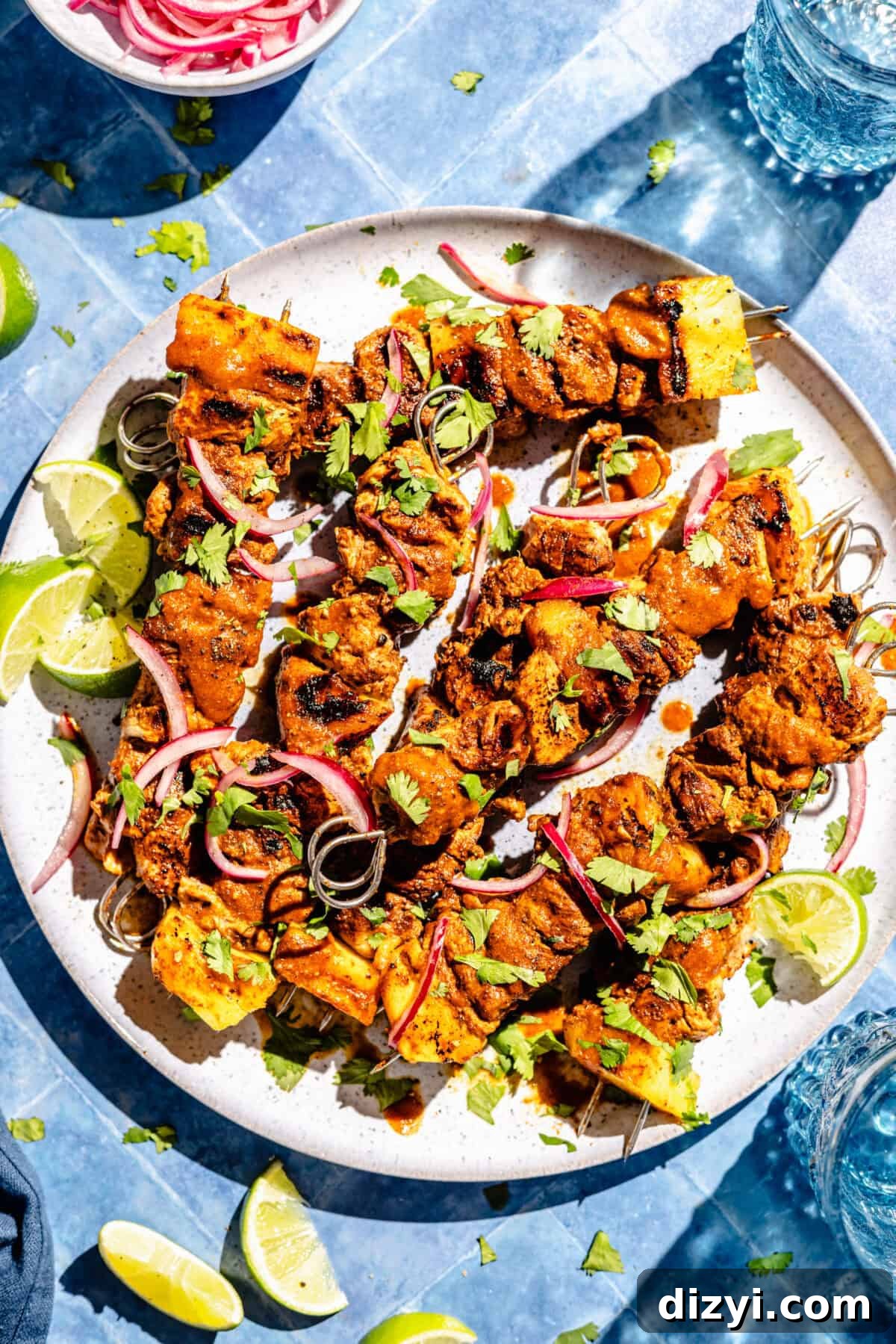 Pork Pastor Skewers assembled on plate. Limes and pickled onions scattered around.